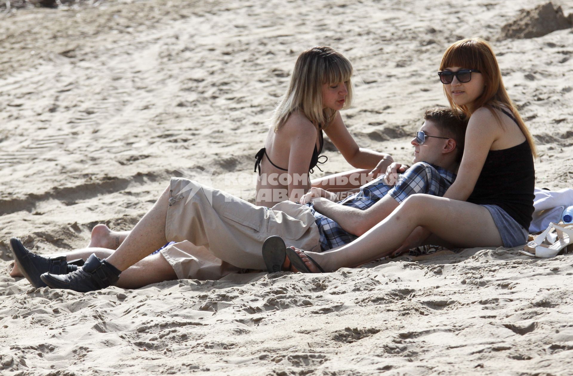 Пляж молодой парень в окружении двух девушек на песчаном пляже.