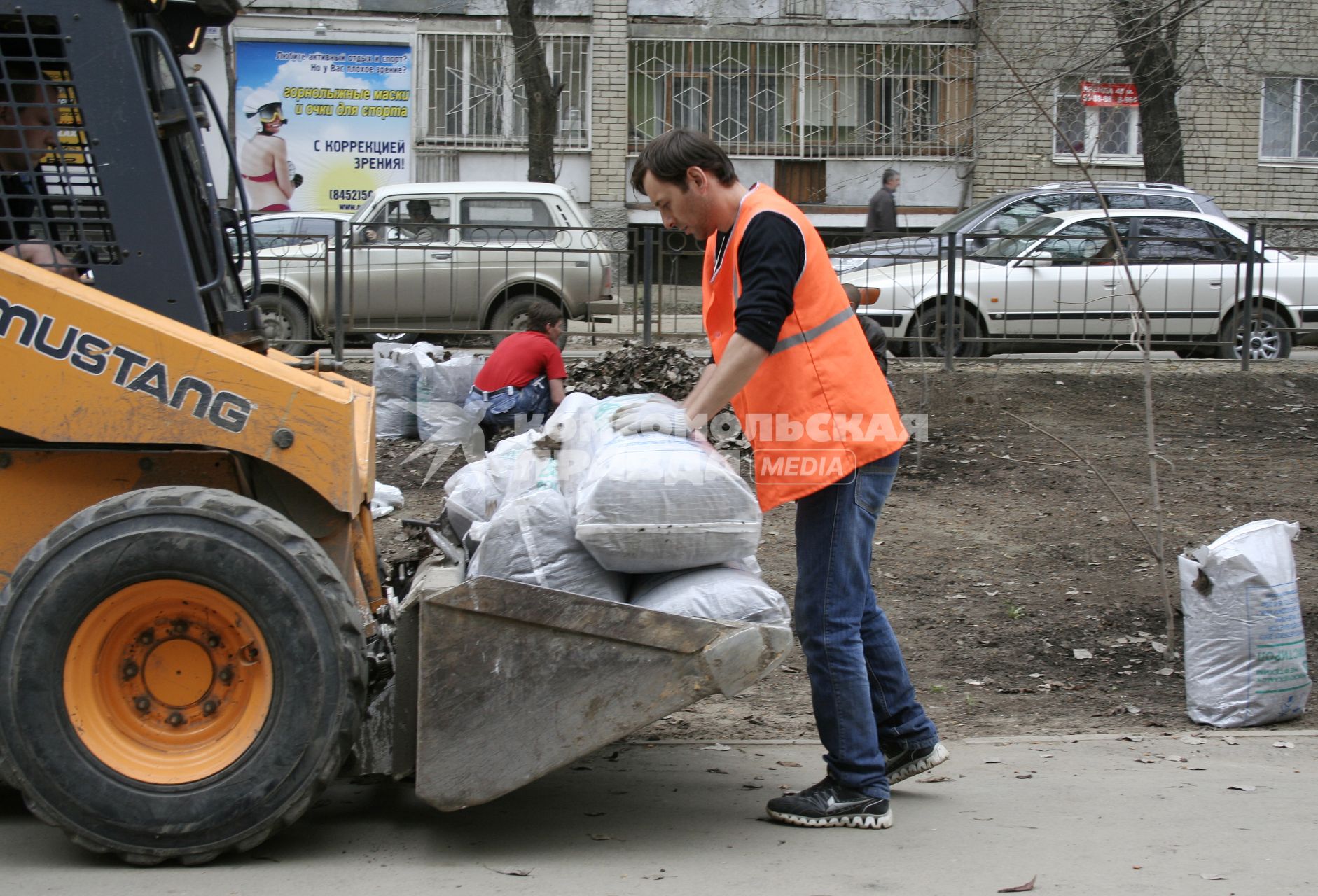 Мужчина складывает мешки с собранной прошлогодней листвой на погрузчик.