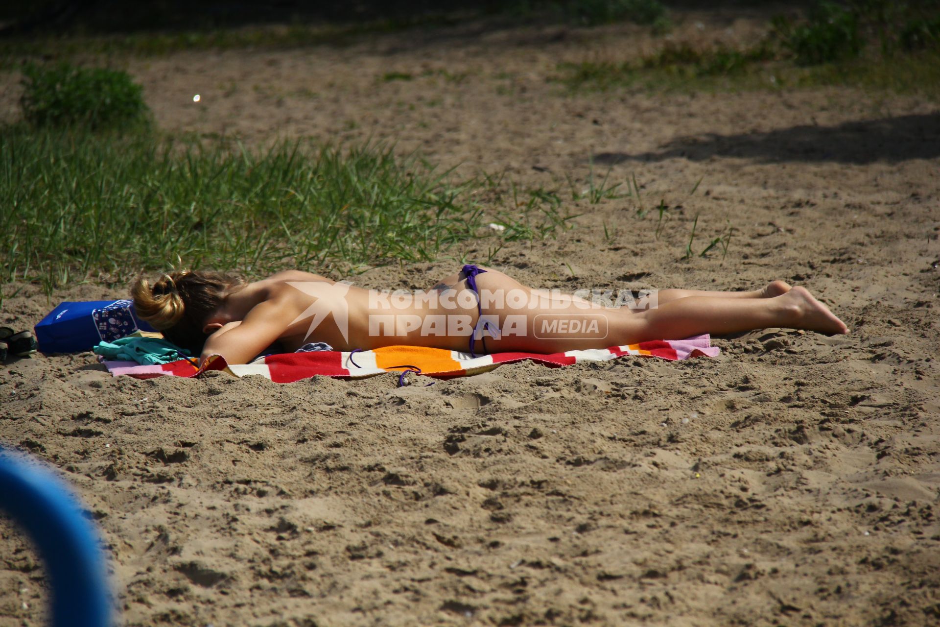 Девушка загорает на пляже сняв верхнюю часть купальника.