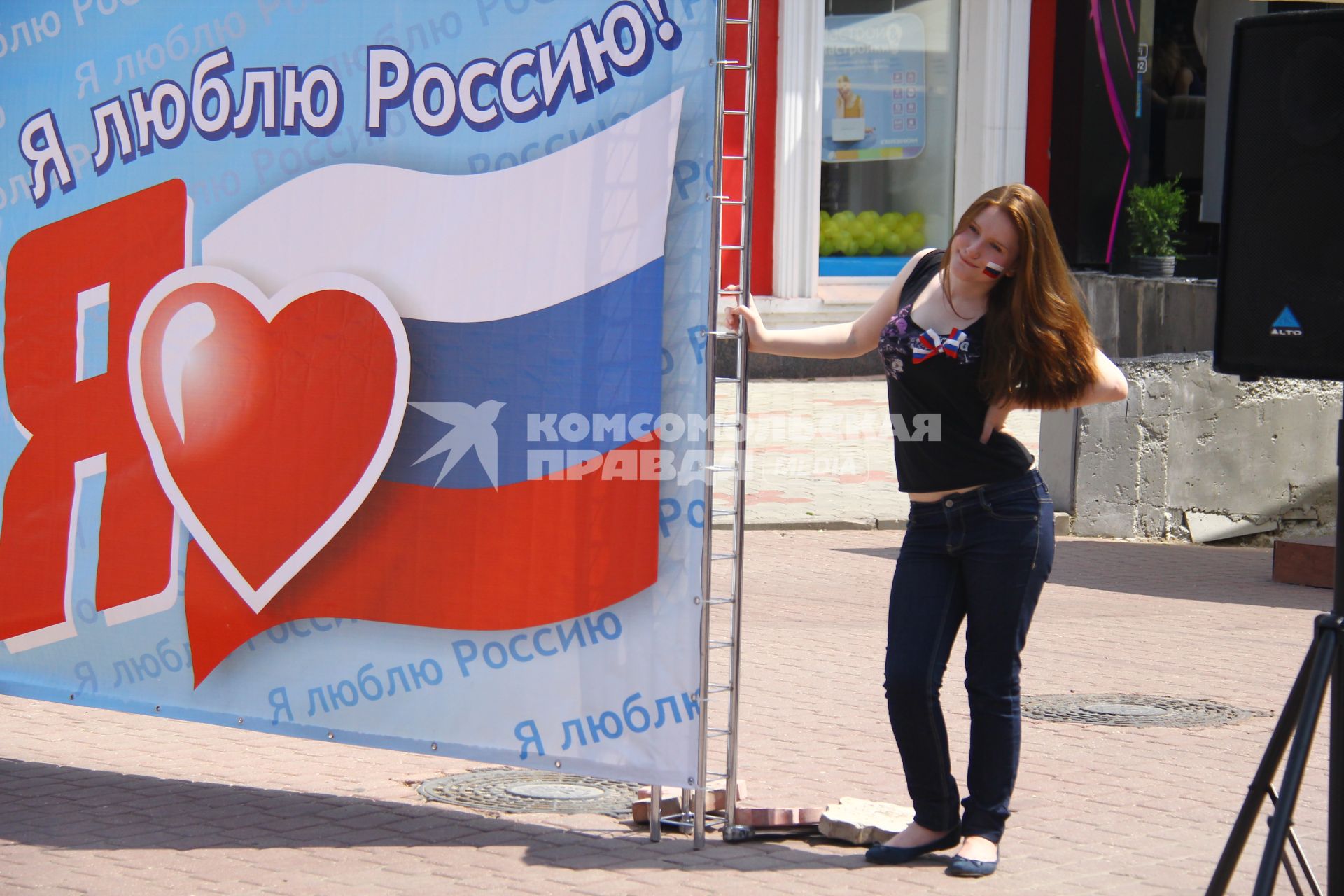 Люди отмечают праздник День России в Нижнем Новгороде. Девушка стоит на фоне плаката с надписью `Я люблю Россию!`.