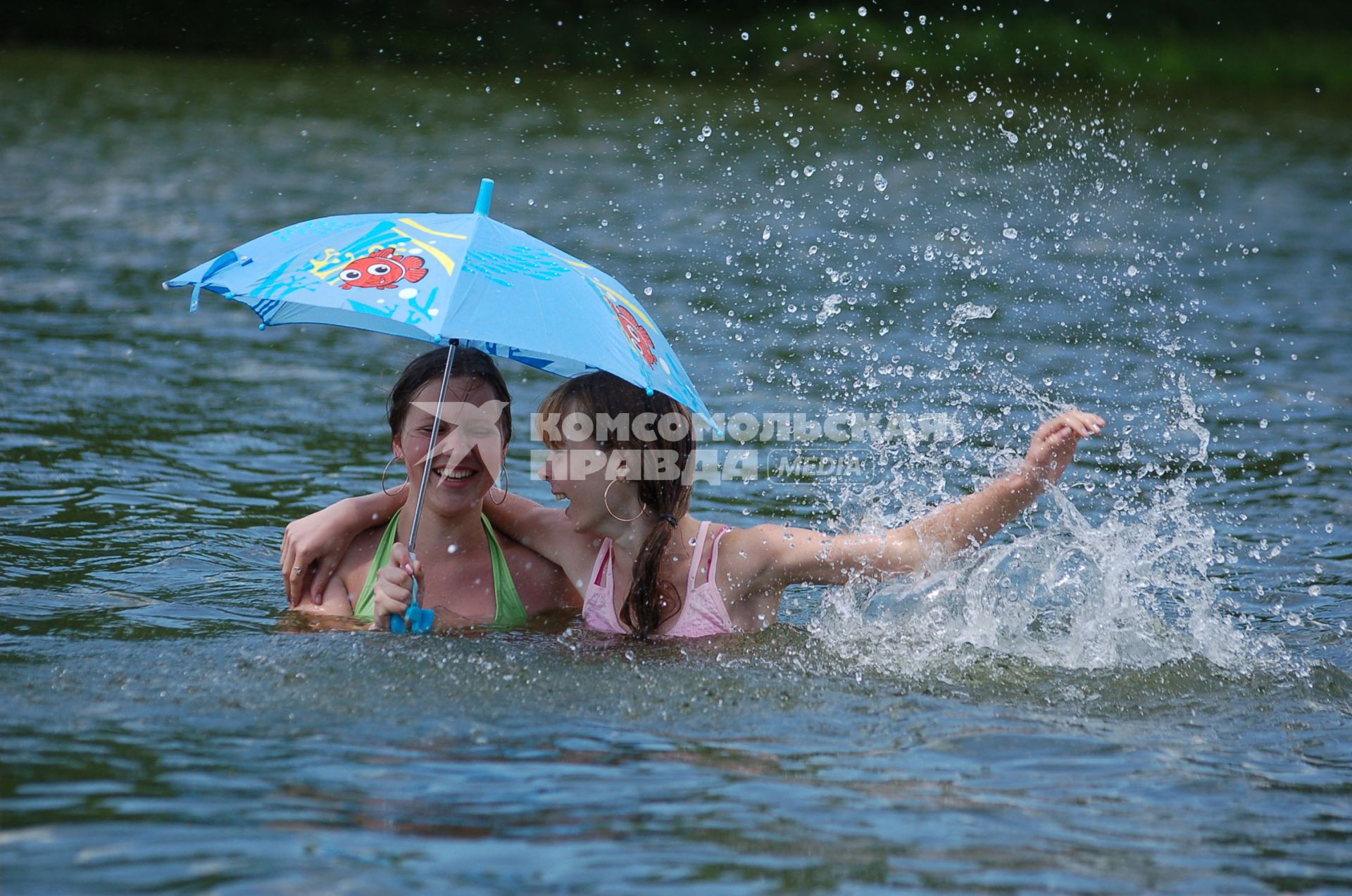 Две молодые девушки купаются в водоеме под зонтом.