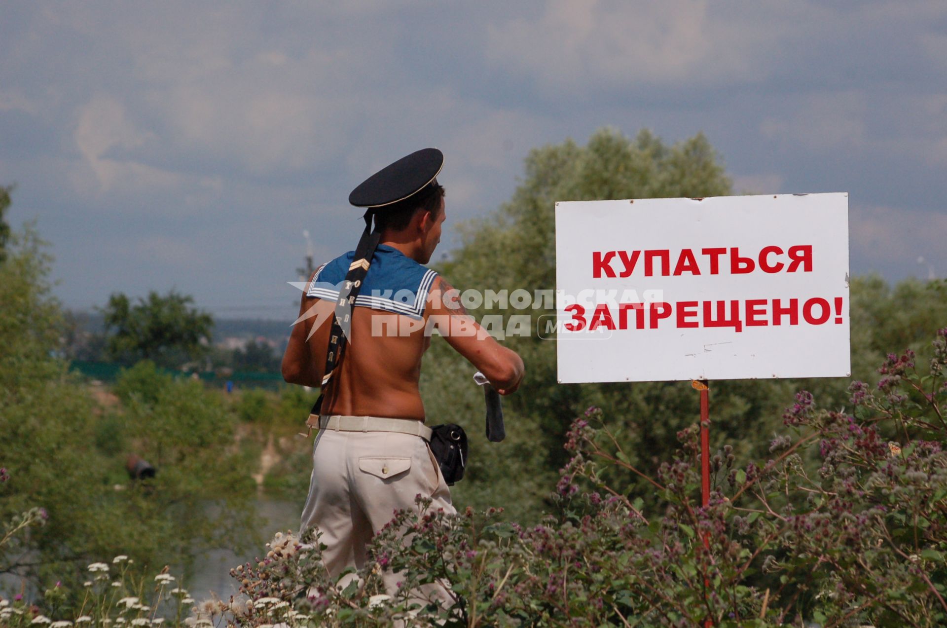 Молодой человек в бескозырке рядом с объявлением о запрете купания.