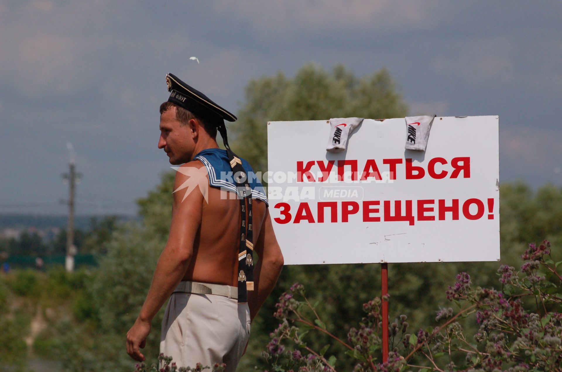 Молодой человек в бескозырке рядом с объявлением о запрете купания.