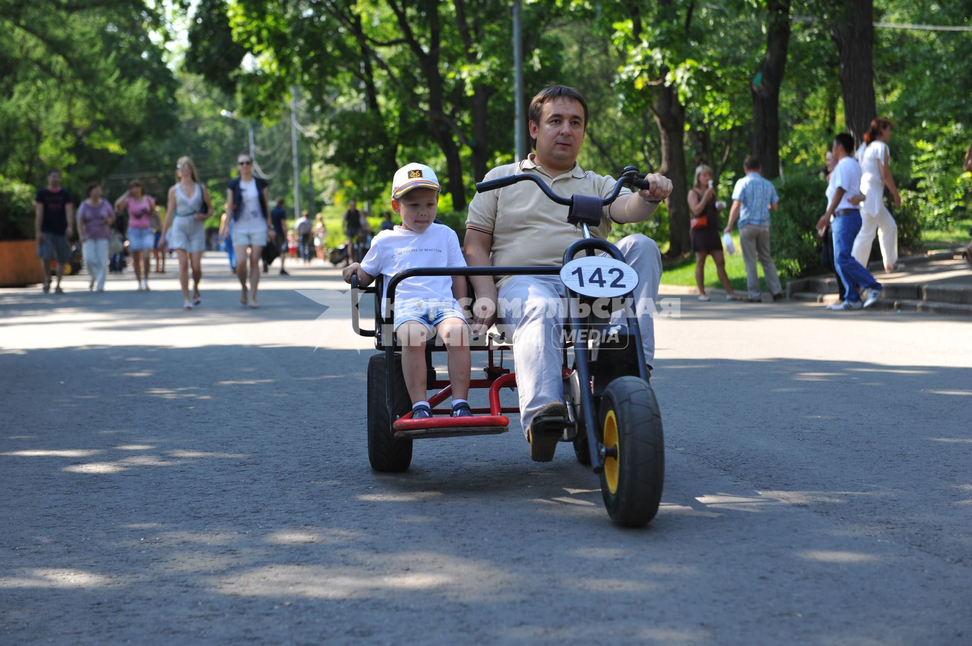 Парк `Сокольники`. На снимке: мужчина с ребенком катаются на велосипеде по парку.