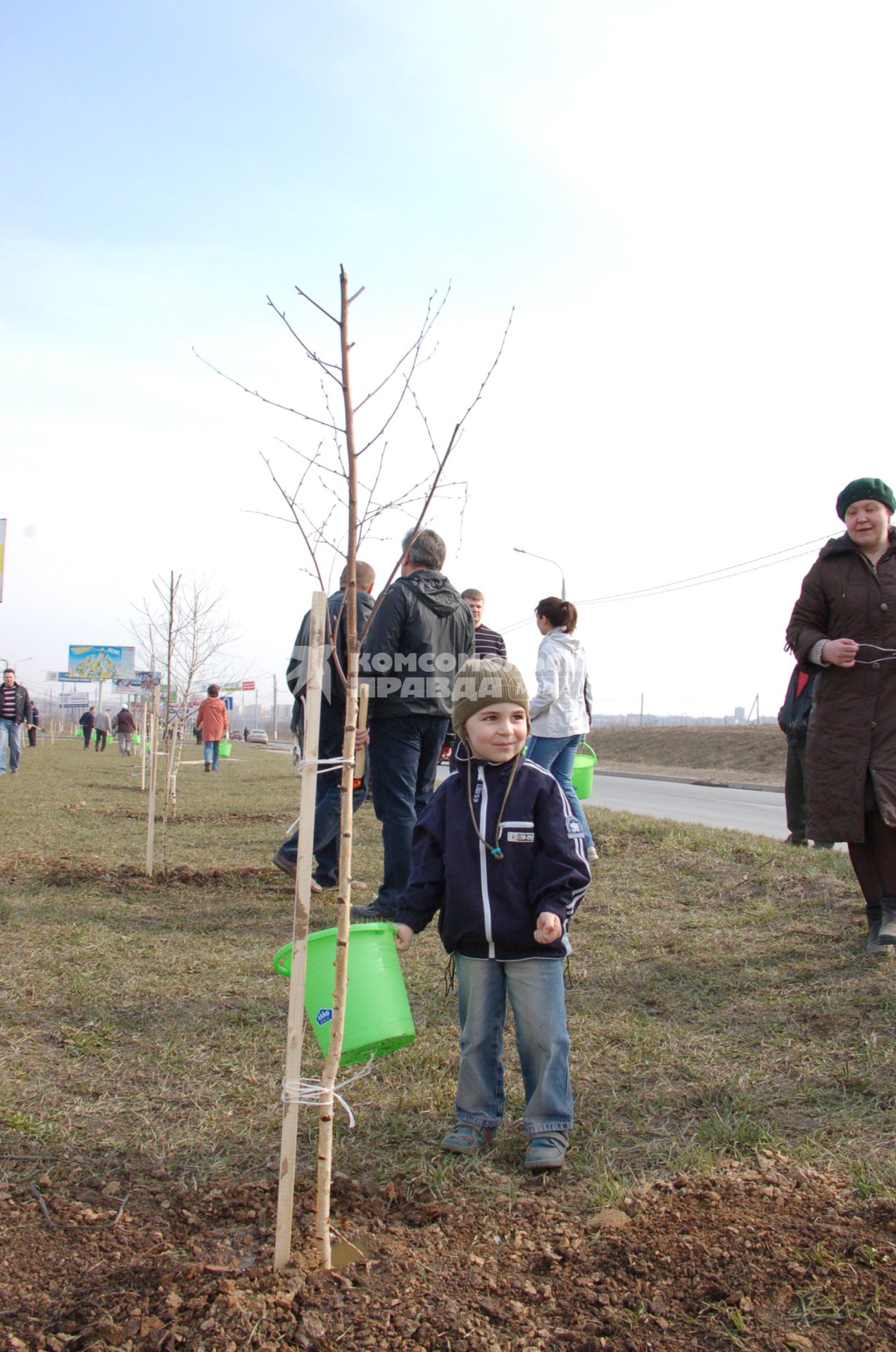 Ребенок поливает только что посаженный саженец дерева из ведра.