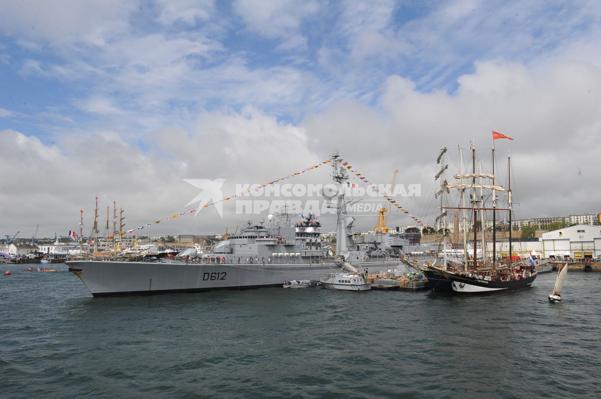 Военный корабль (слева) и корабль со спущенными парусами стоят у причала в порту .