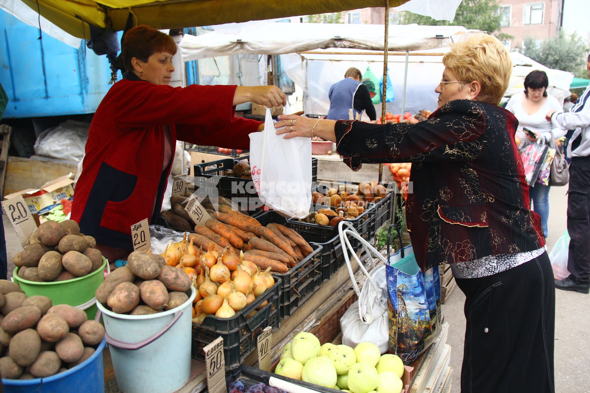 Женщина покупает продукты на овощном рынке.