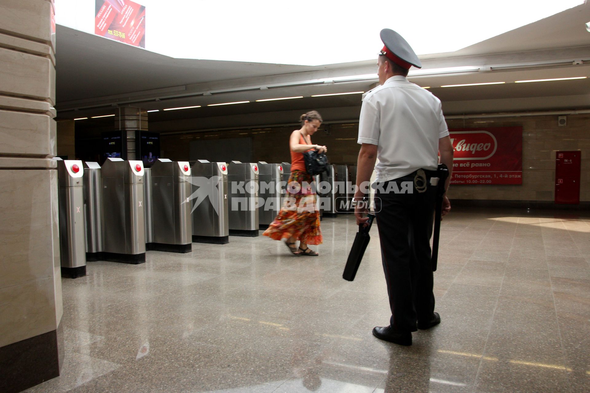 Полицейские в метро проводят операцию `Антитеррор`. На снимке: Полицейский стоит на входе в метро с дубинкой и металлоискателем. Девушка прошла турникет.