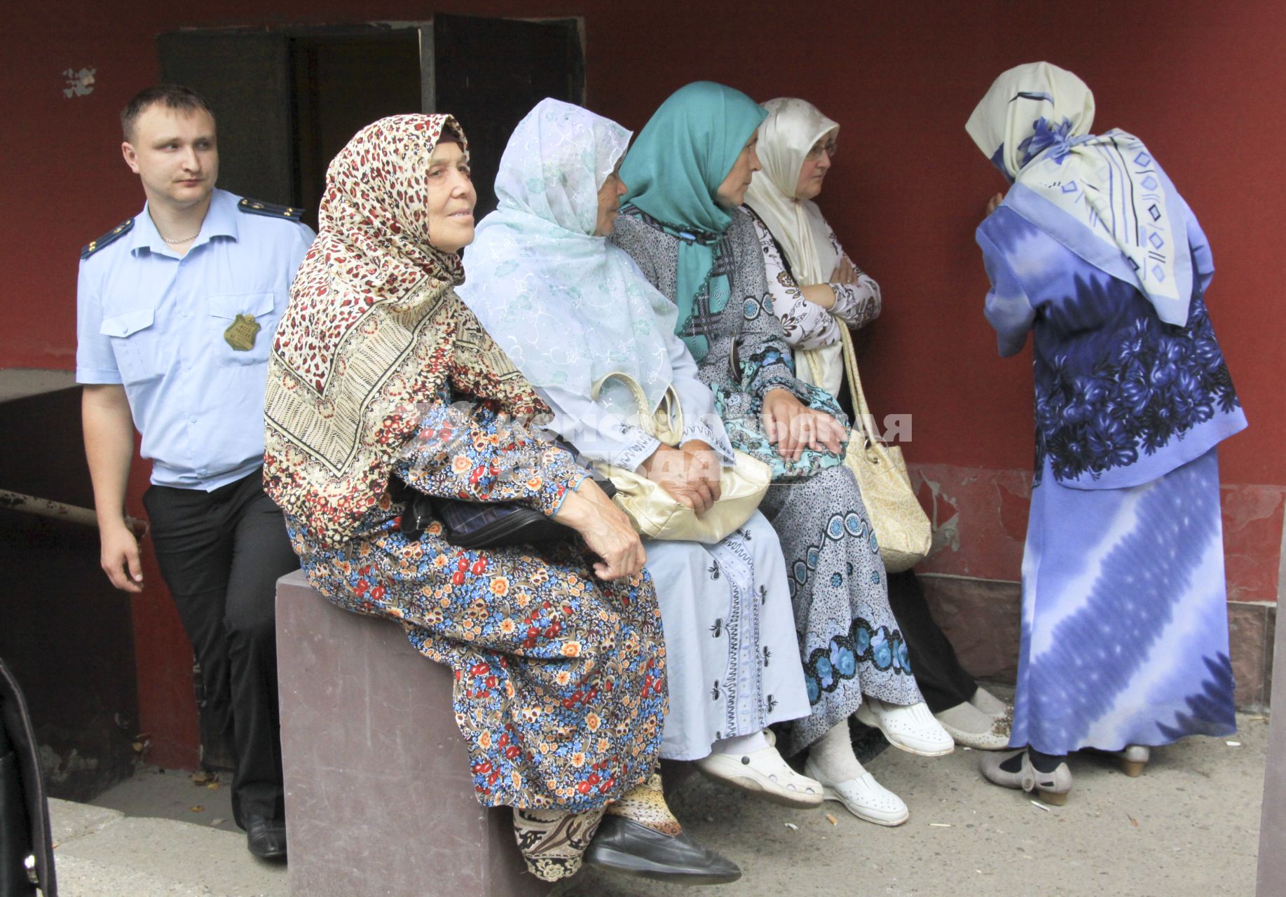 Мусульманки в хиджабах сидят у здания суда, из здания выходит судебный пристав.