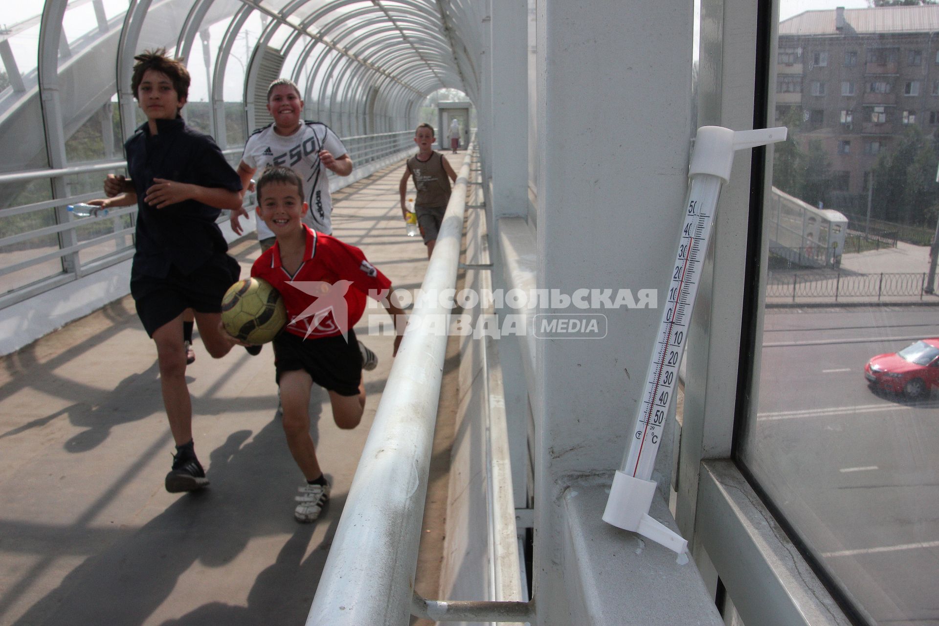 Жара +40 градусов в пешеходном переходе. По переходу бегут мальчики в спортивной форме с футбольным мячом.