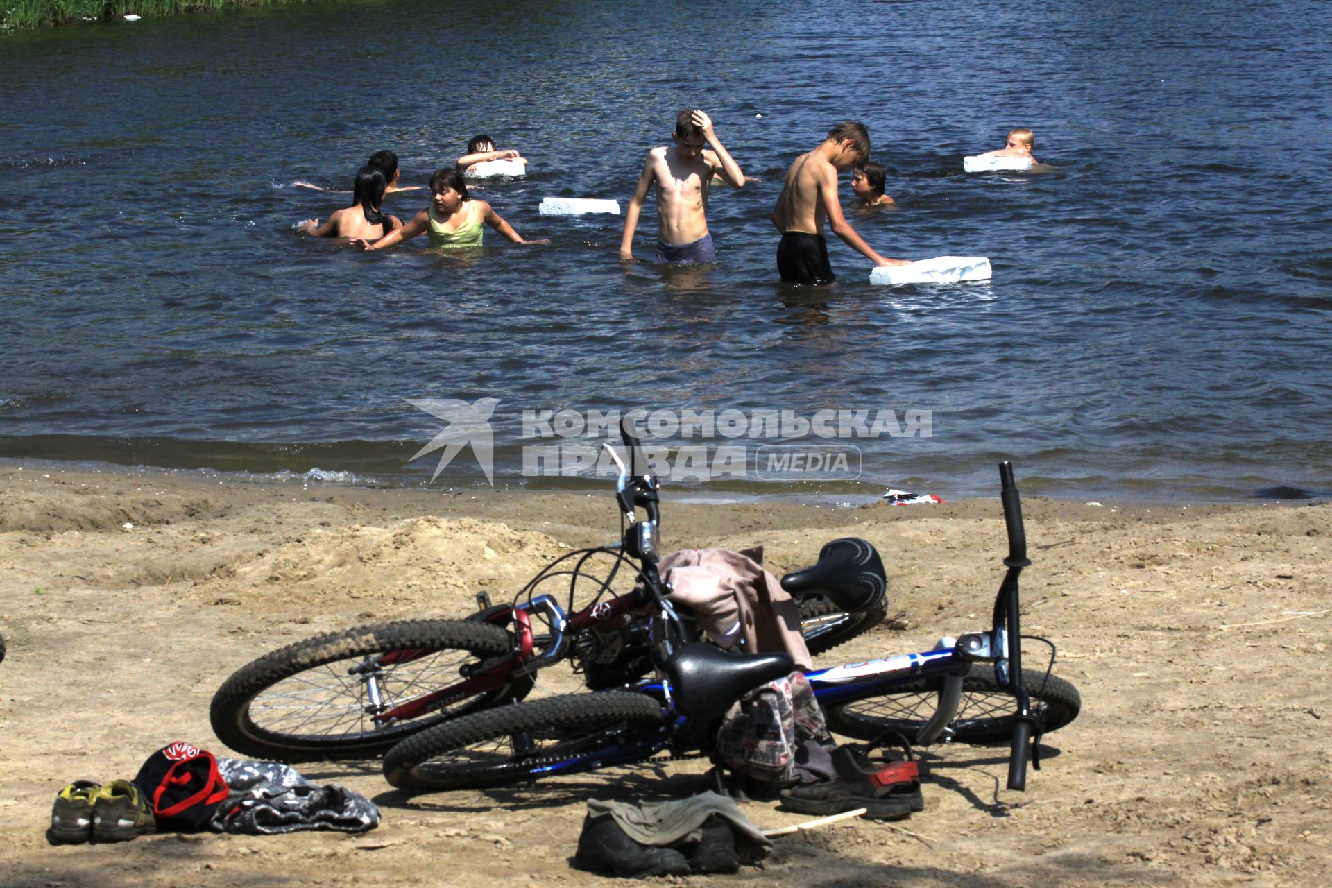 Дети купаются в воде, на берегу лежат велосипеды.