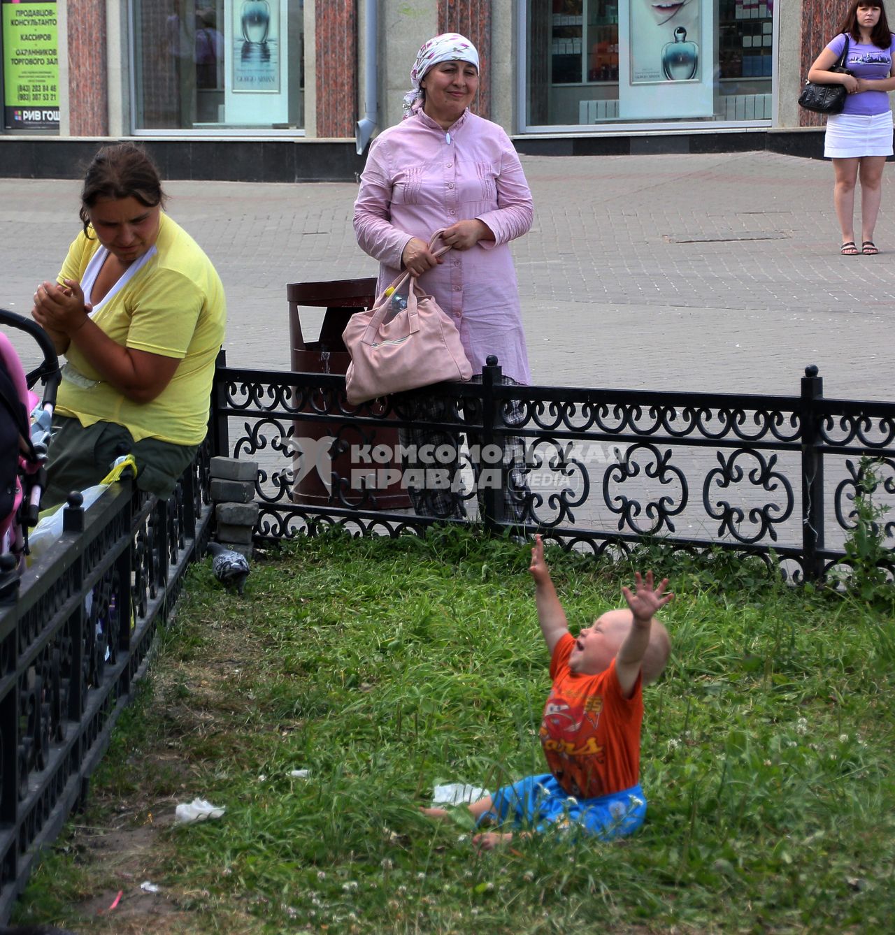 Маленький ребенок сидит на траве, плачет подняв руки вверх.