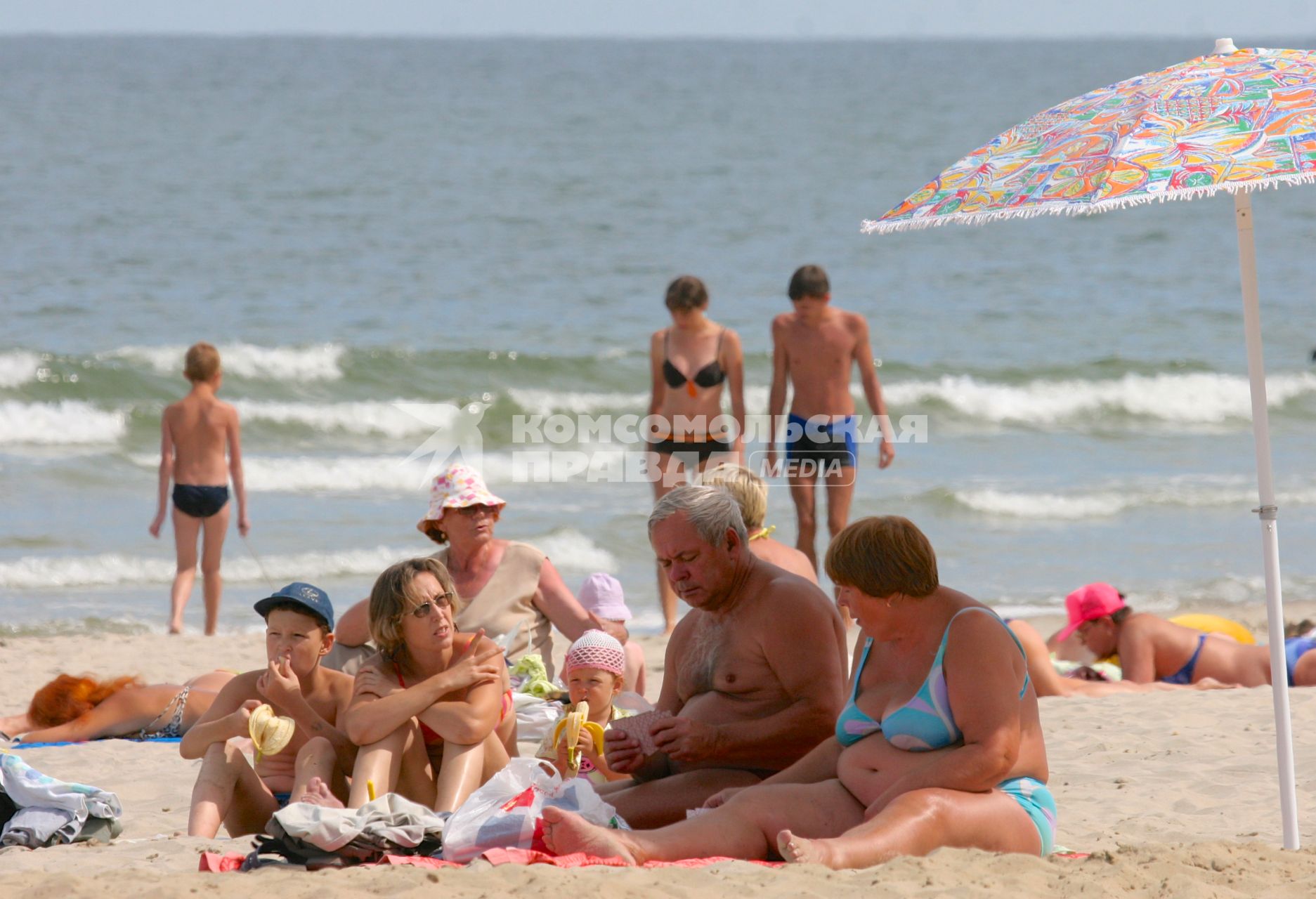 Семья отдыхает на морском пляже перекусывает и играет в карты.