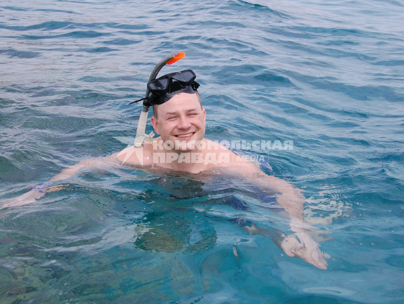 Довольный мужчина в маске для ныряние плавает в морской воде.