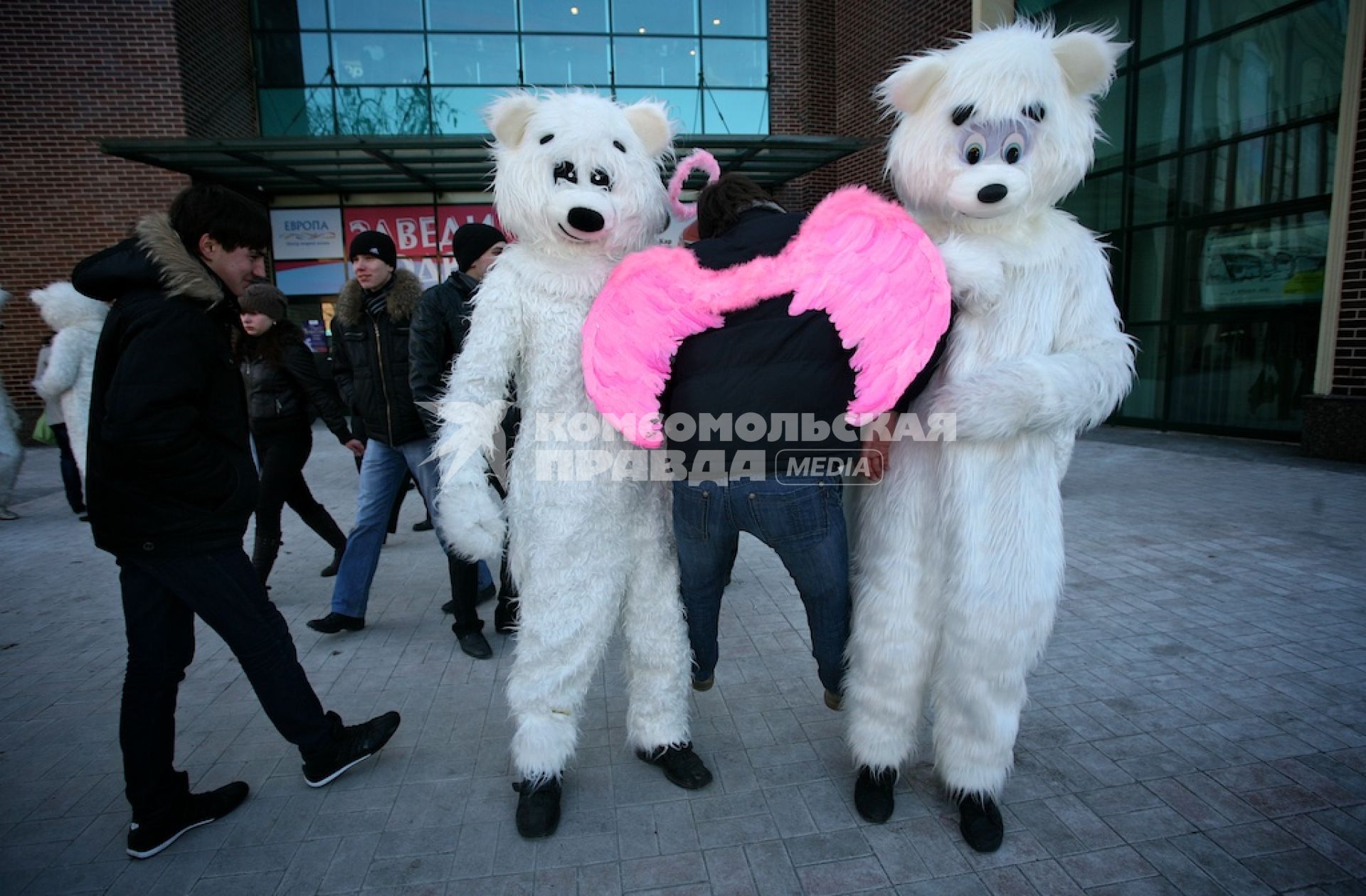 Двое в костюме белых медведей держат под руки мужчину с приклеенными розовыми крыльями на спине.