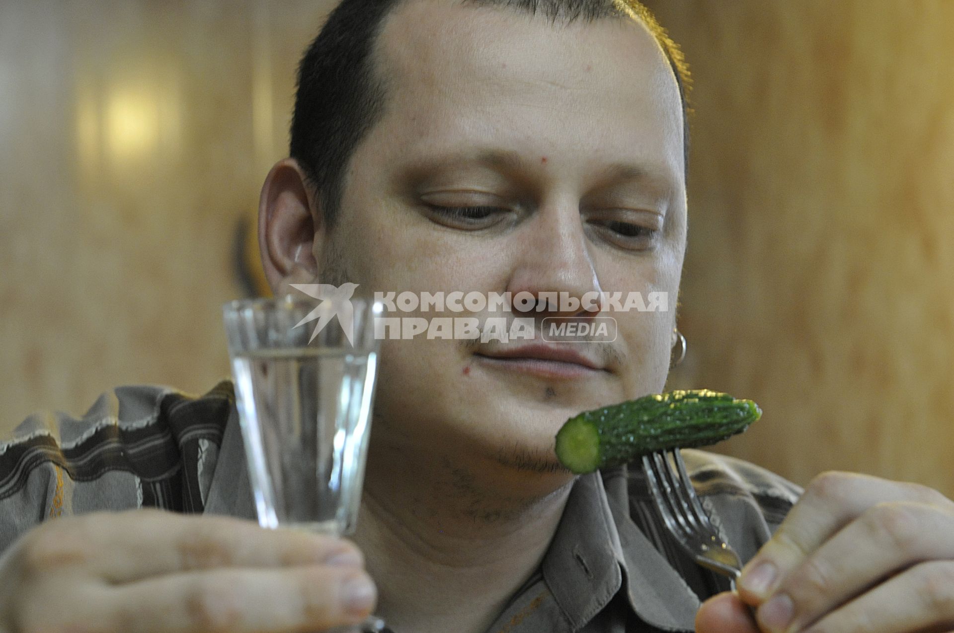 Мужчина с рюмкой водки и малосольным огурцом на вилке.