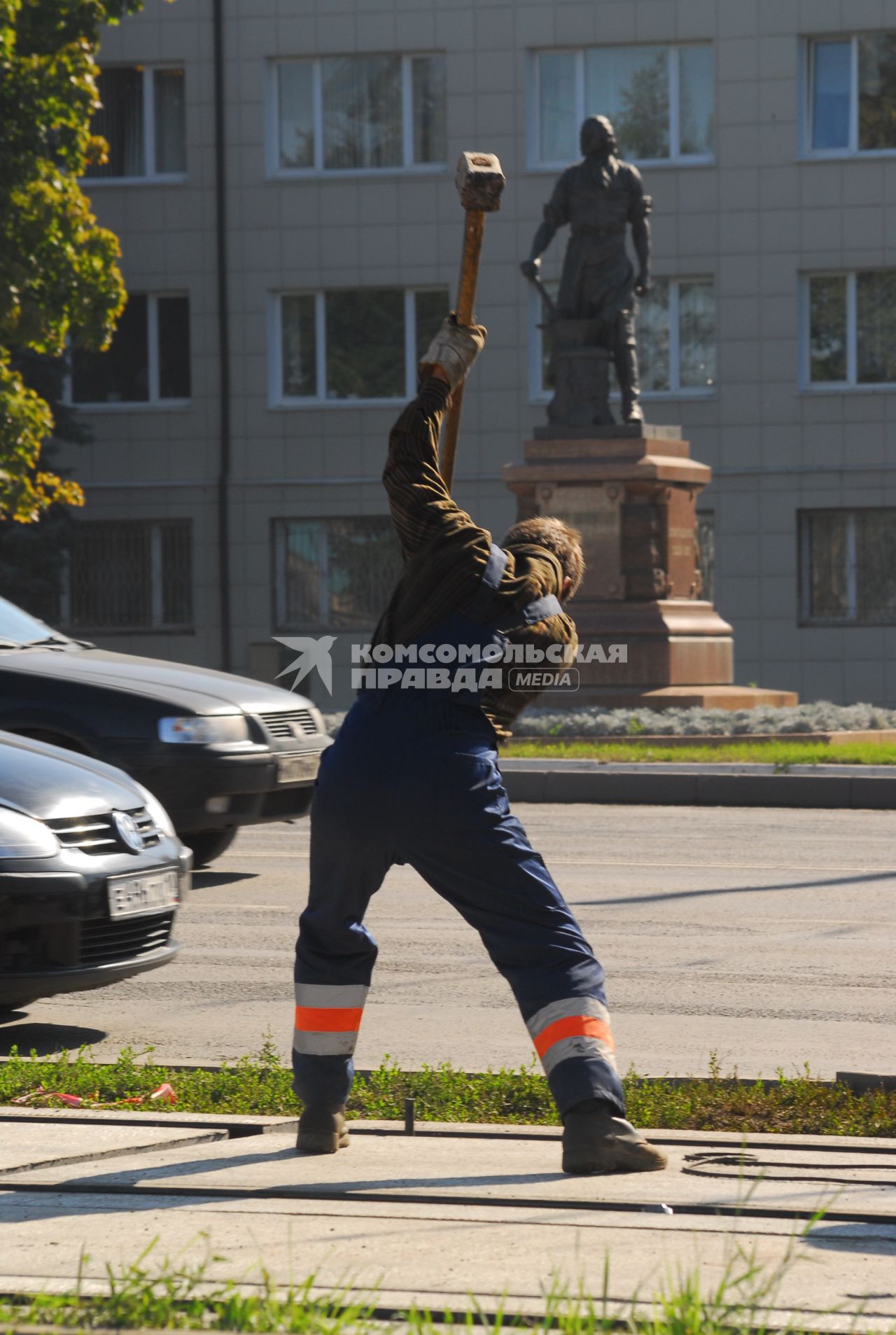 Дорожный рабочий с кувалдой на фоне памятники Петру I у Тульского оружейного завода.