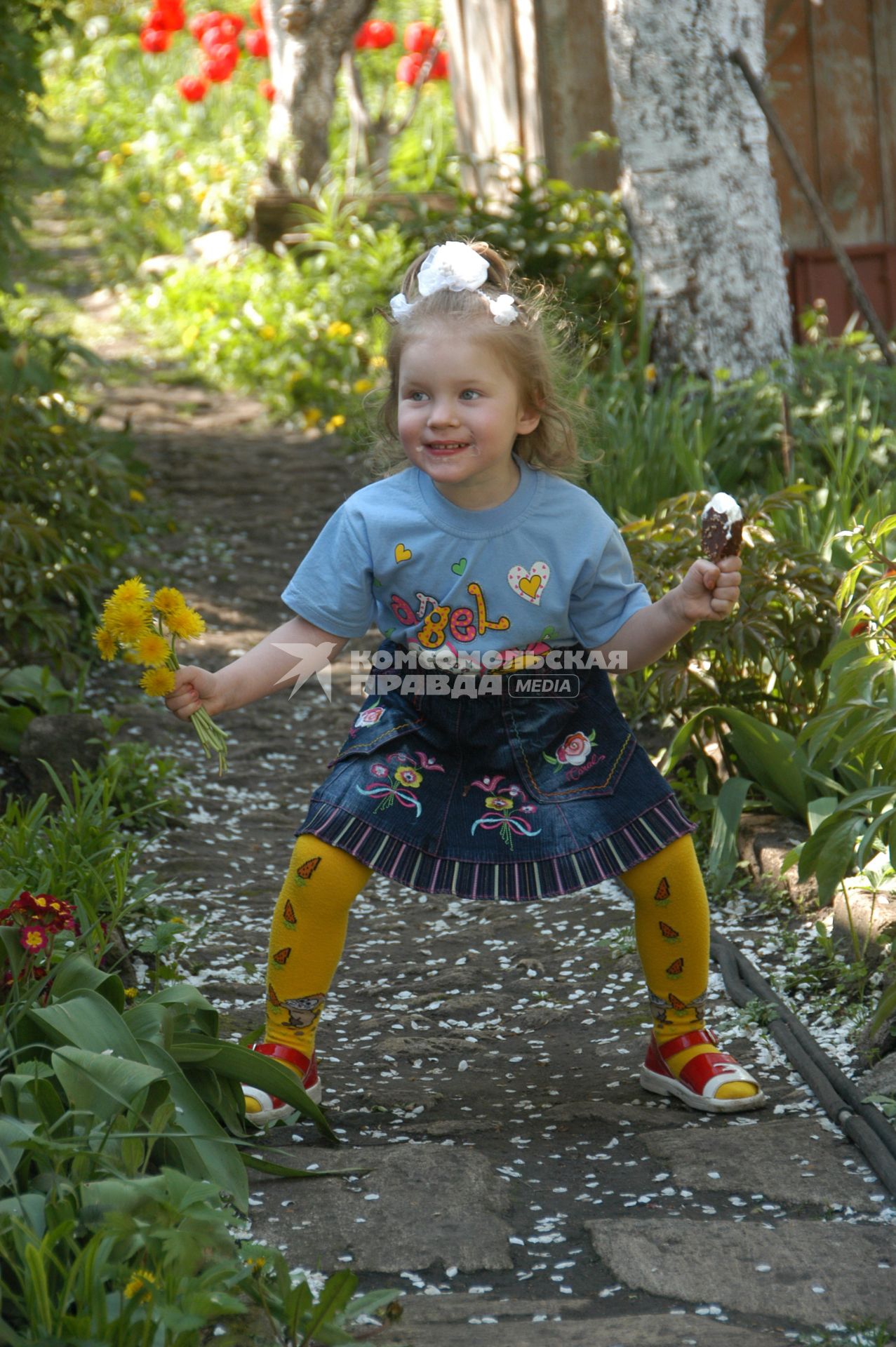 Девочка с мороженным и букетом одуванчиков играет на даче.