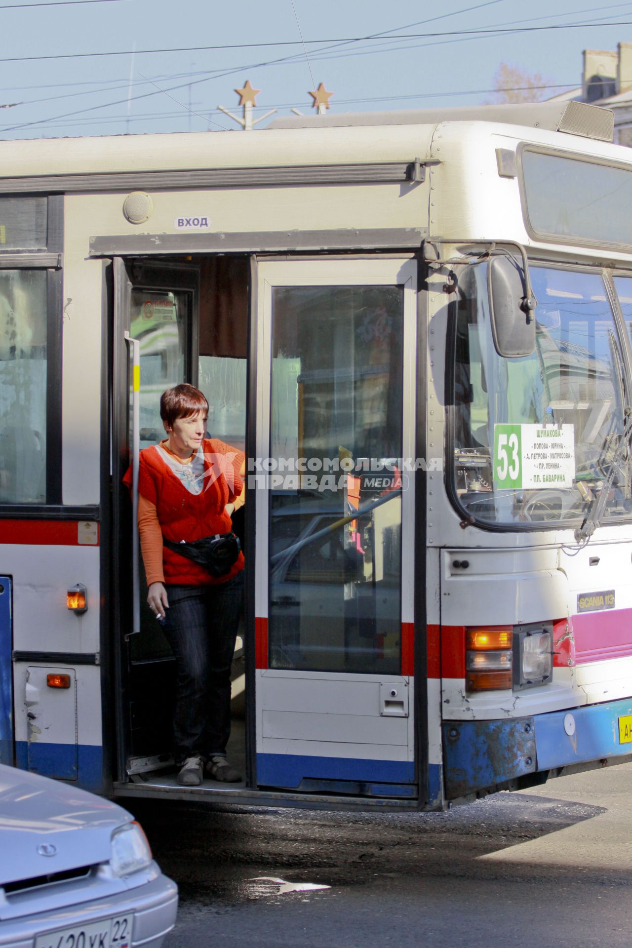 Женщина водитель общественного транспорта перекуривает в открытых дверях стоя в пробке на дороге.