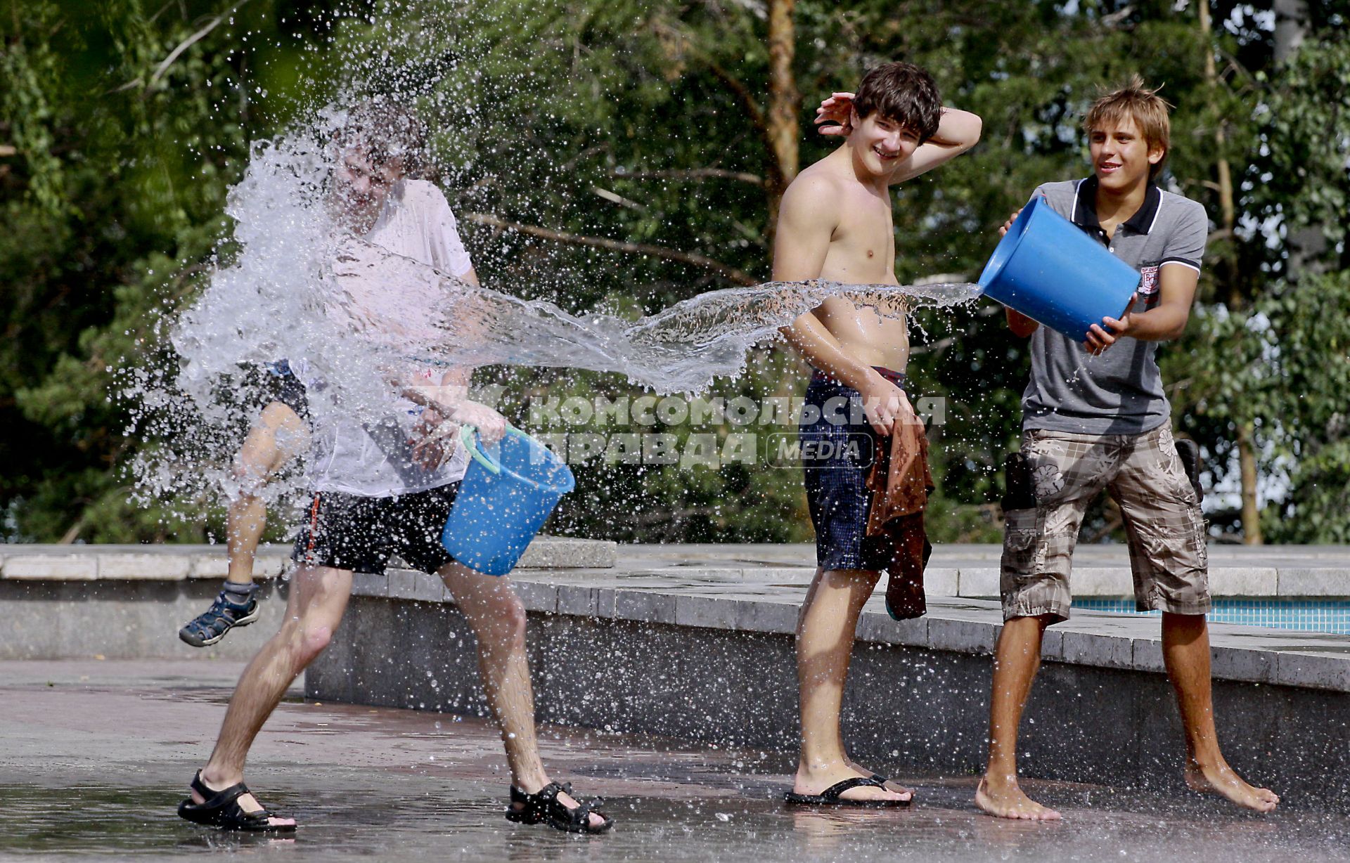 Подростки обливаются водой около фонтана.