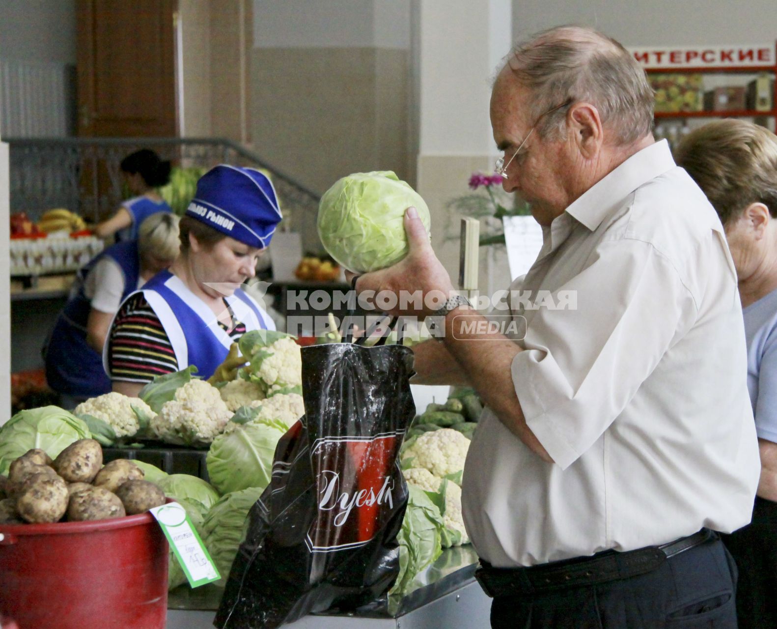 Покупатель покупает капусту на рынке в ряду торговцев овощами.