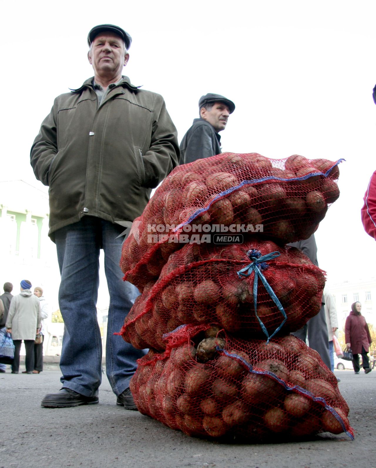 Продавец овощей стоит рядом с сетками картофеля.