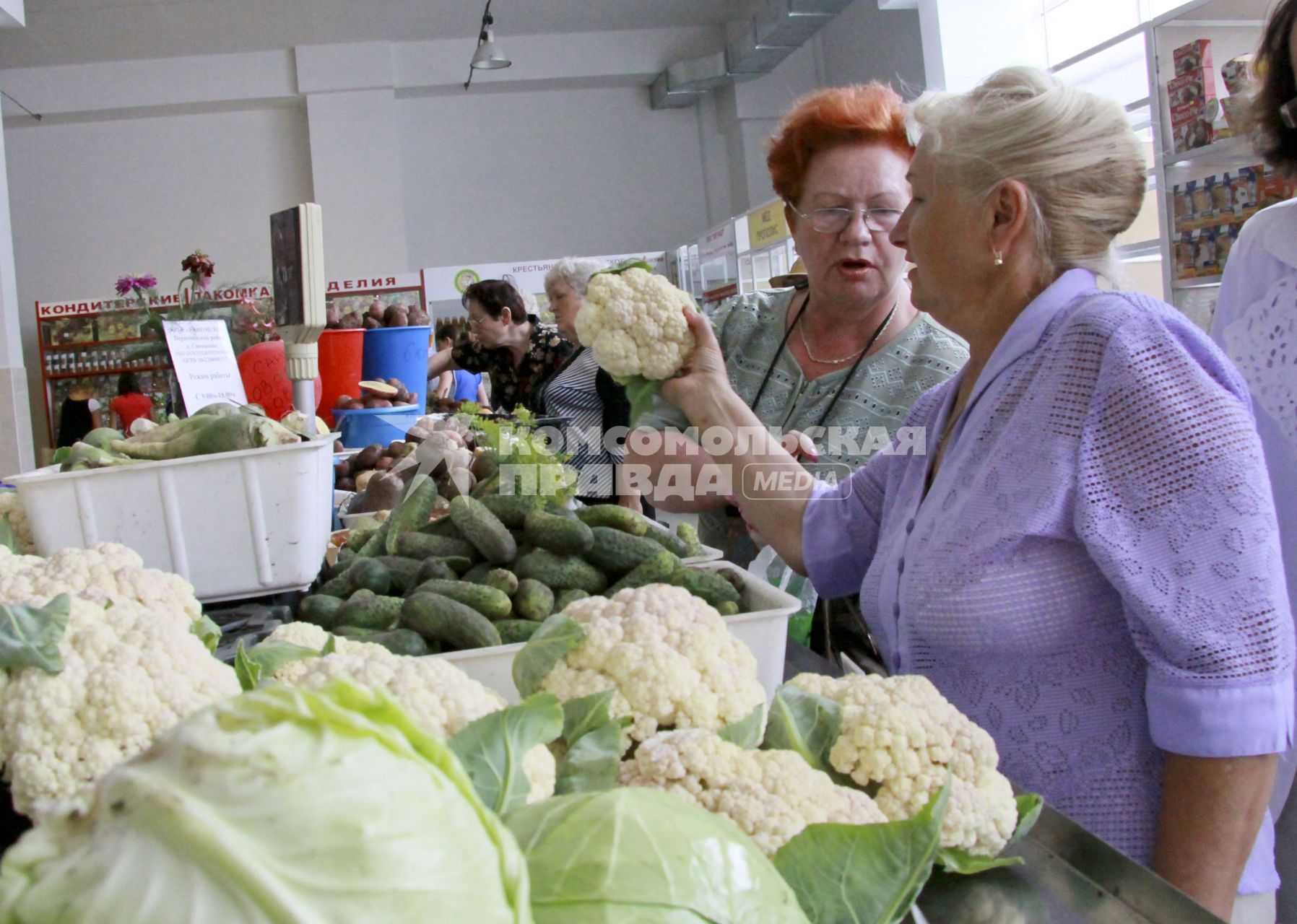 Женщины выбирают капусту на рынке в ряду торговцев овощами.