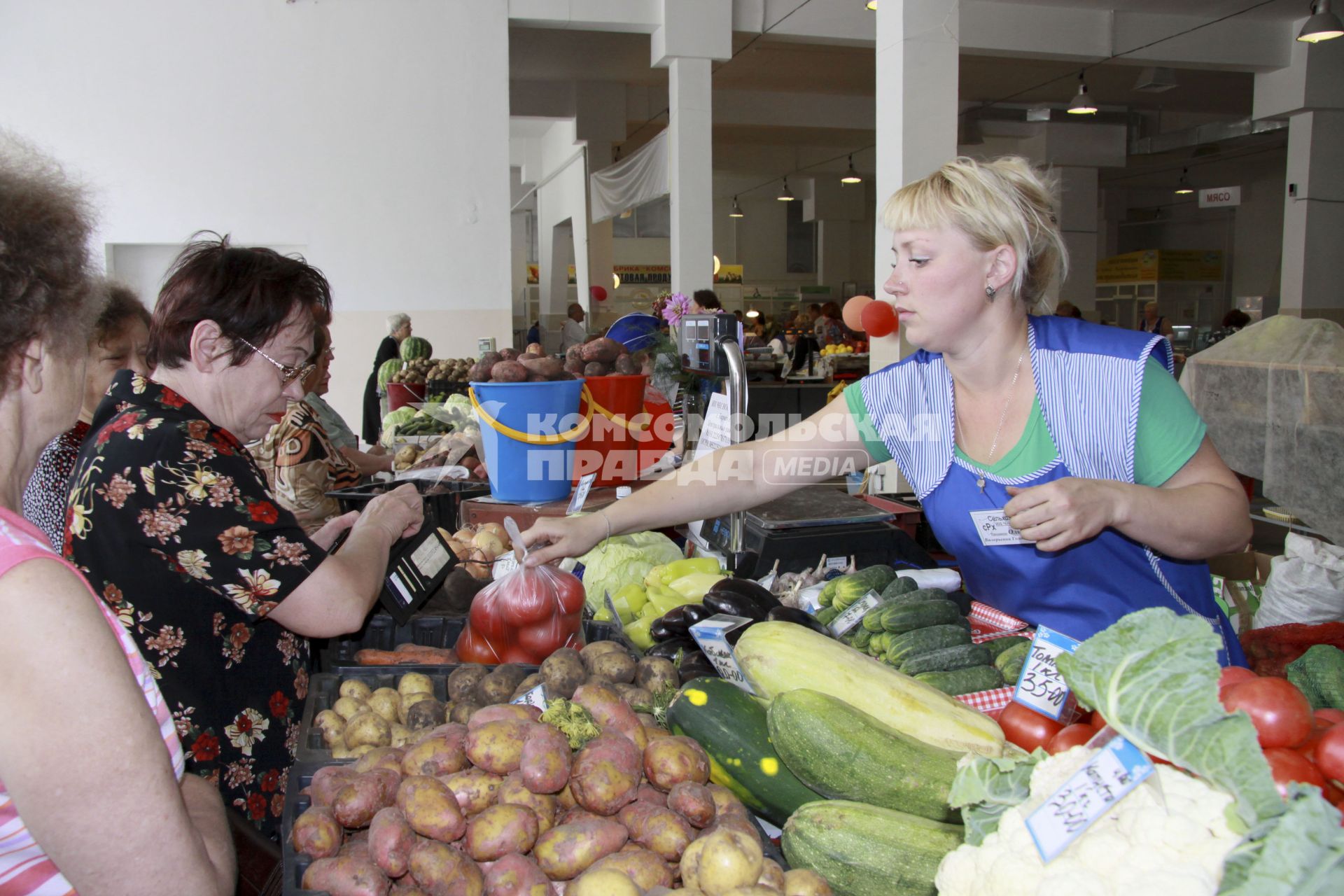 Торговля овощами на рынке. Продавец передает покупателю пакет с помидорами.