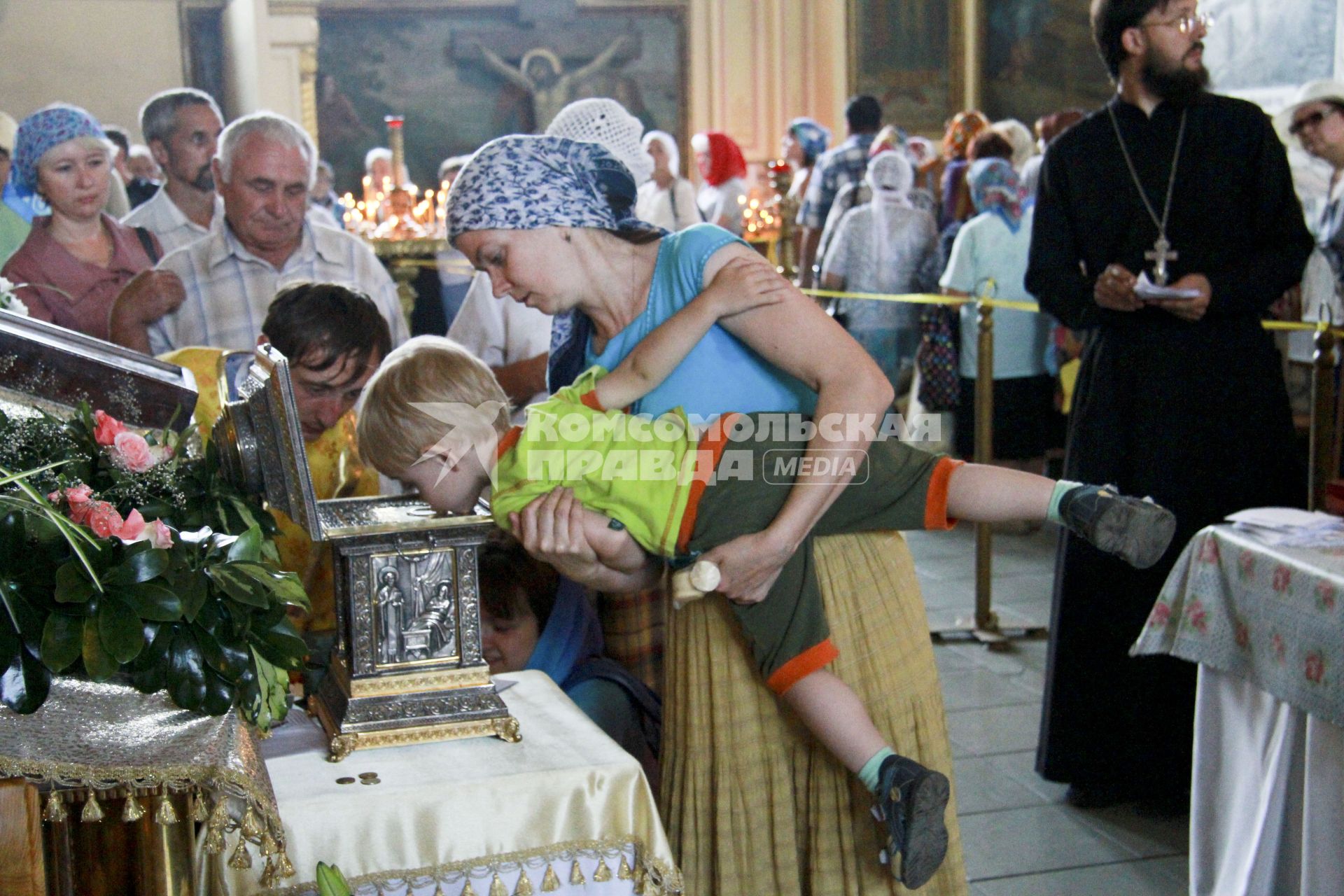 Женщина держит на руках мальчика. Мальчик целует ковчег с мощами Николая Чудотворца в Покровском соборе Барнаула.