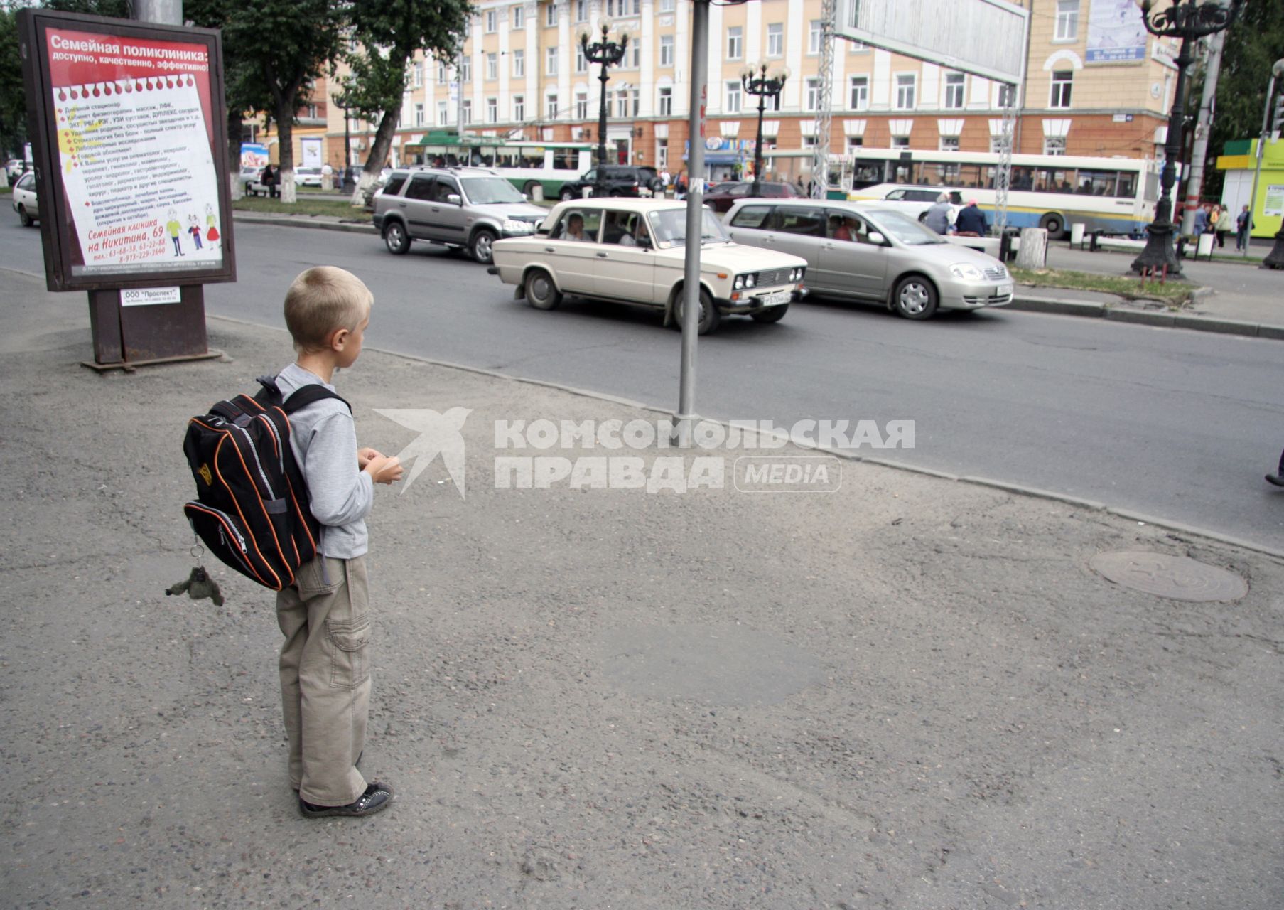 Школьник с портфелем стоит перед дорогой.