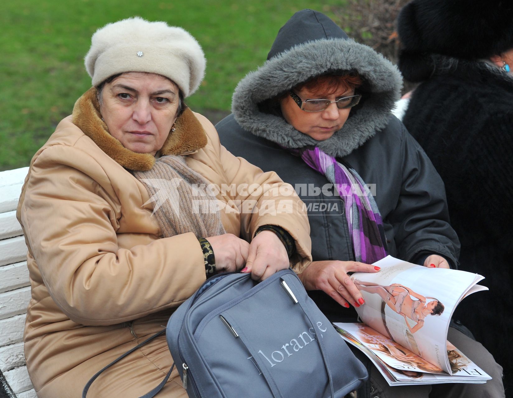 Две немолодые женщины сидят в парке на скамейке, одна из них рассматривает журнал с рекламой нижнего белья.