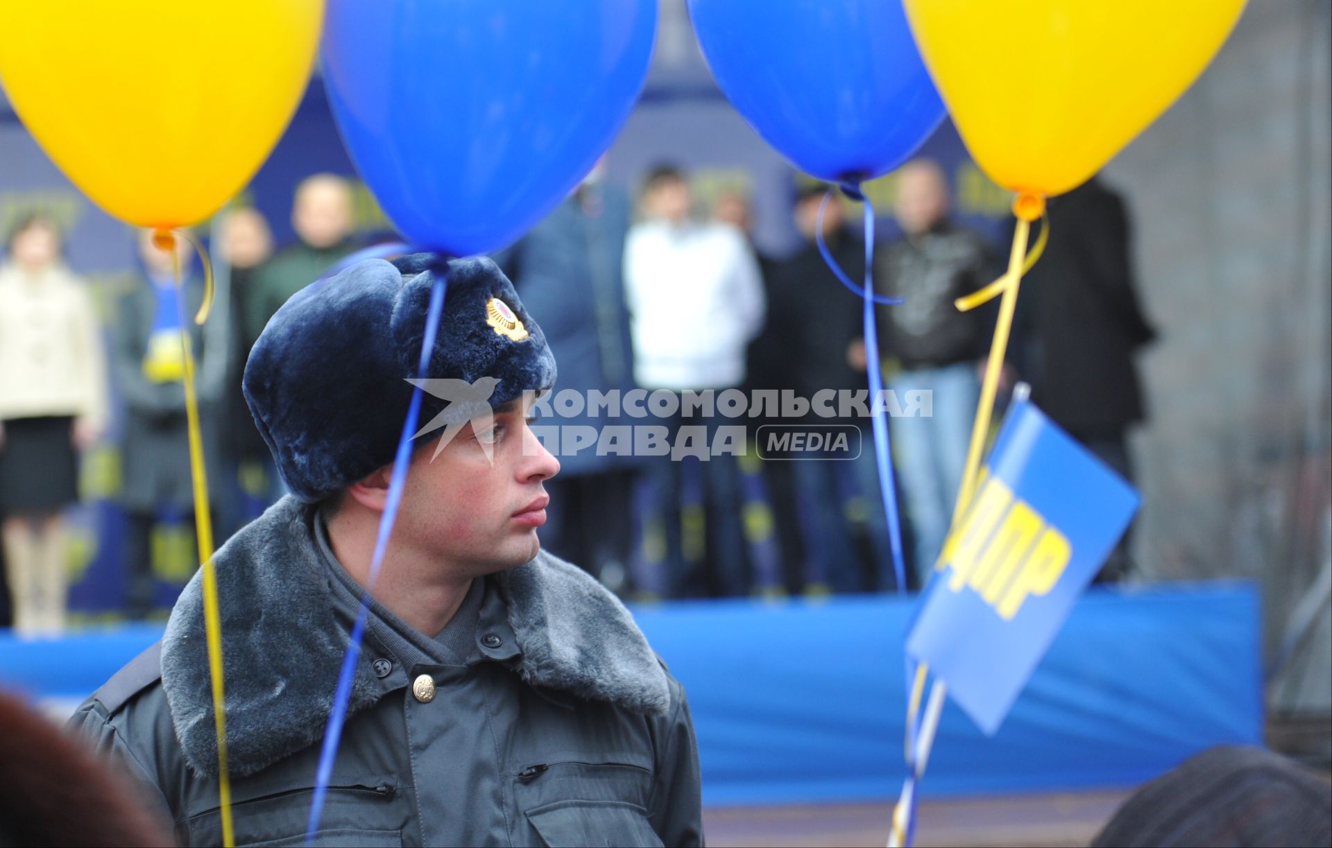 Полицейский стоит в оцеплении на митинге партии `ЛДПР`, рядом с ним висят воздушные шарики.