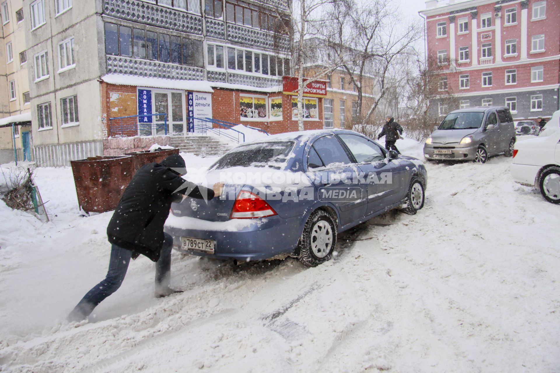 Мужчина толкает застрявший в снегу автомобиль.