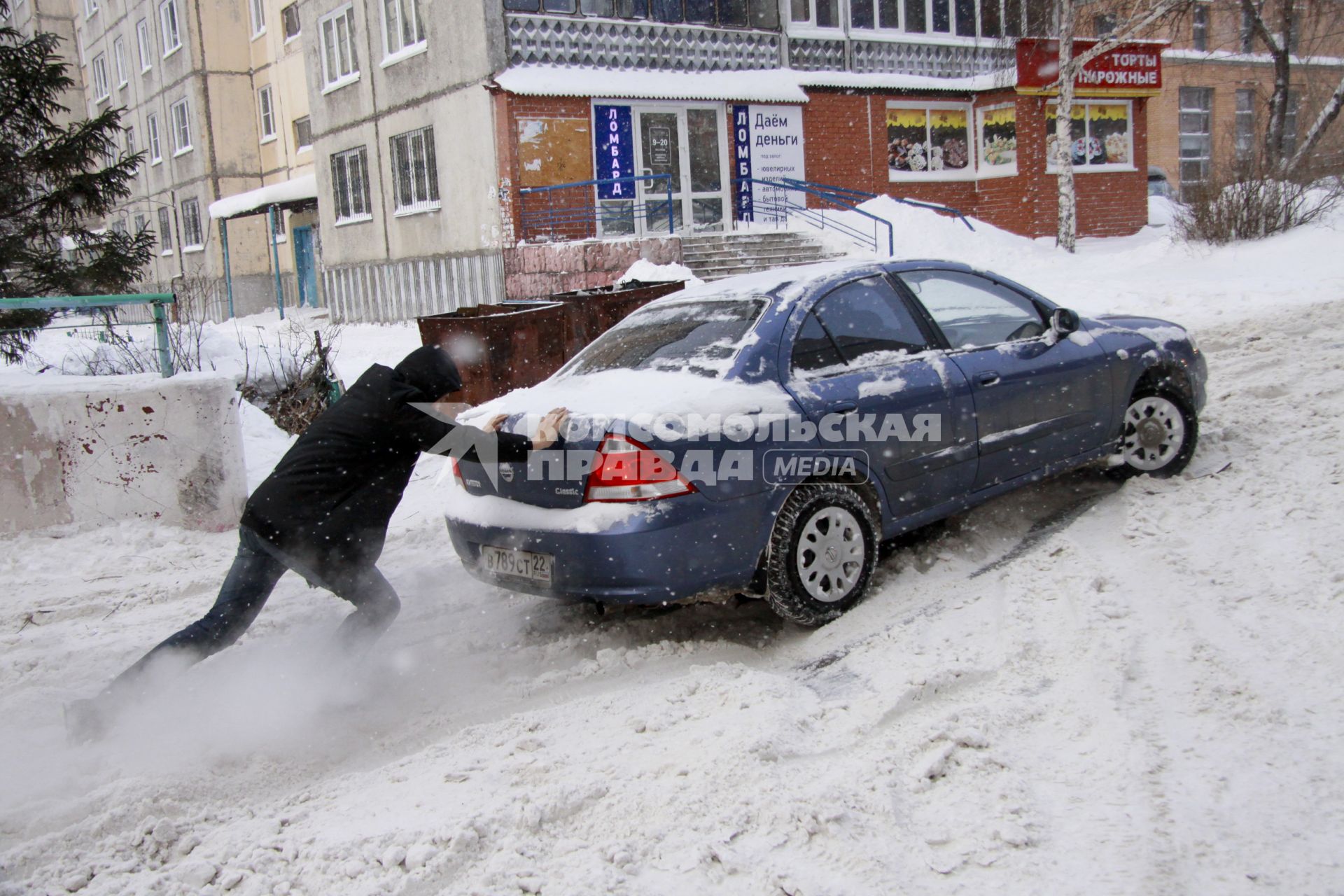 Мужчина толкает застрявший в снегу автомобиль.