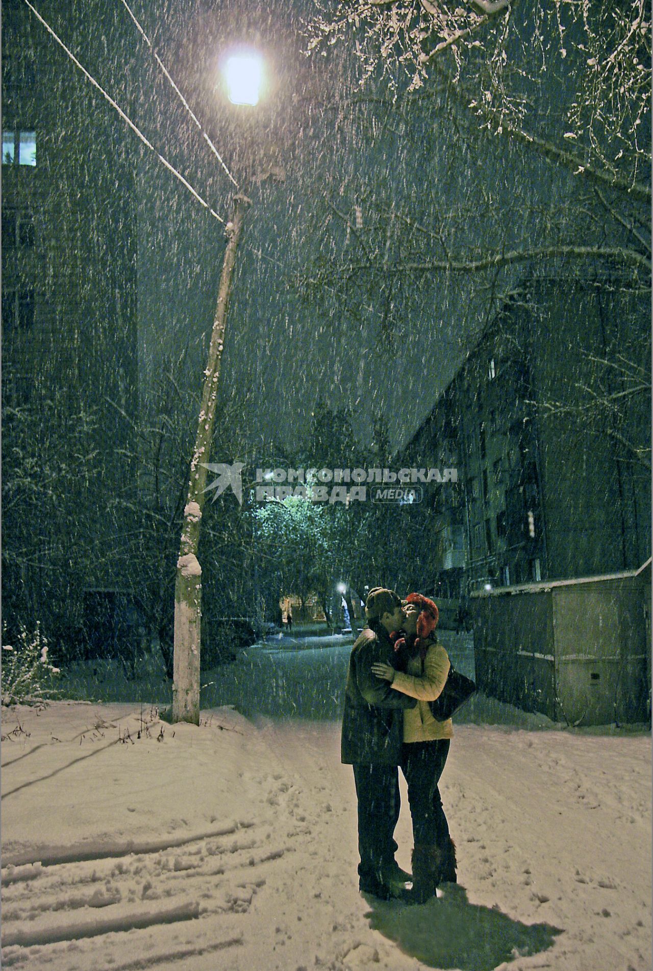 Мужчина и женщина целуются на улице под снегопадом.