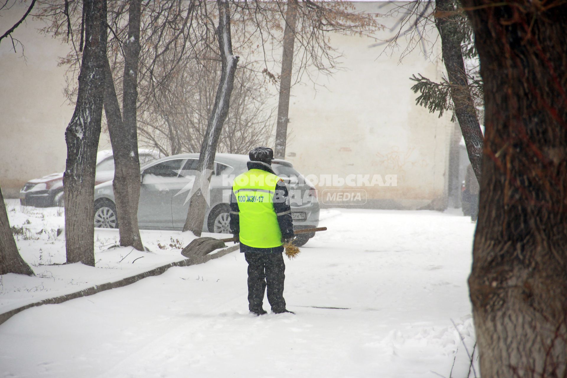 Дворник с лопатой под снегопадом.