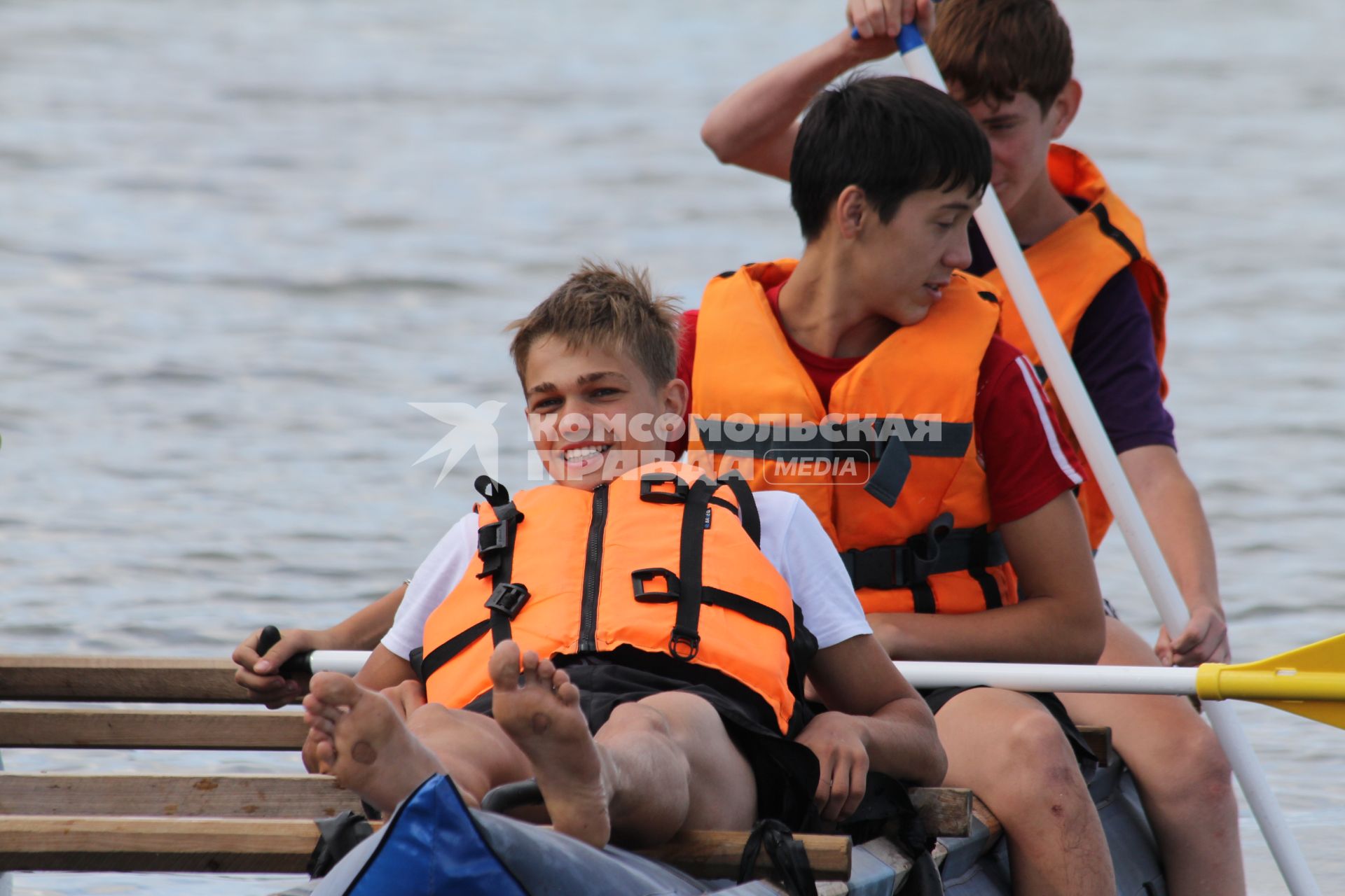 Группа молодых ребят в спасательных жилетах катается на надувном катамаране с веслами.