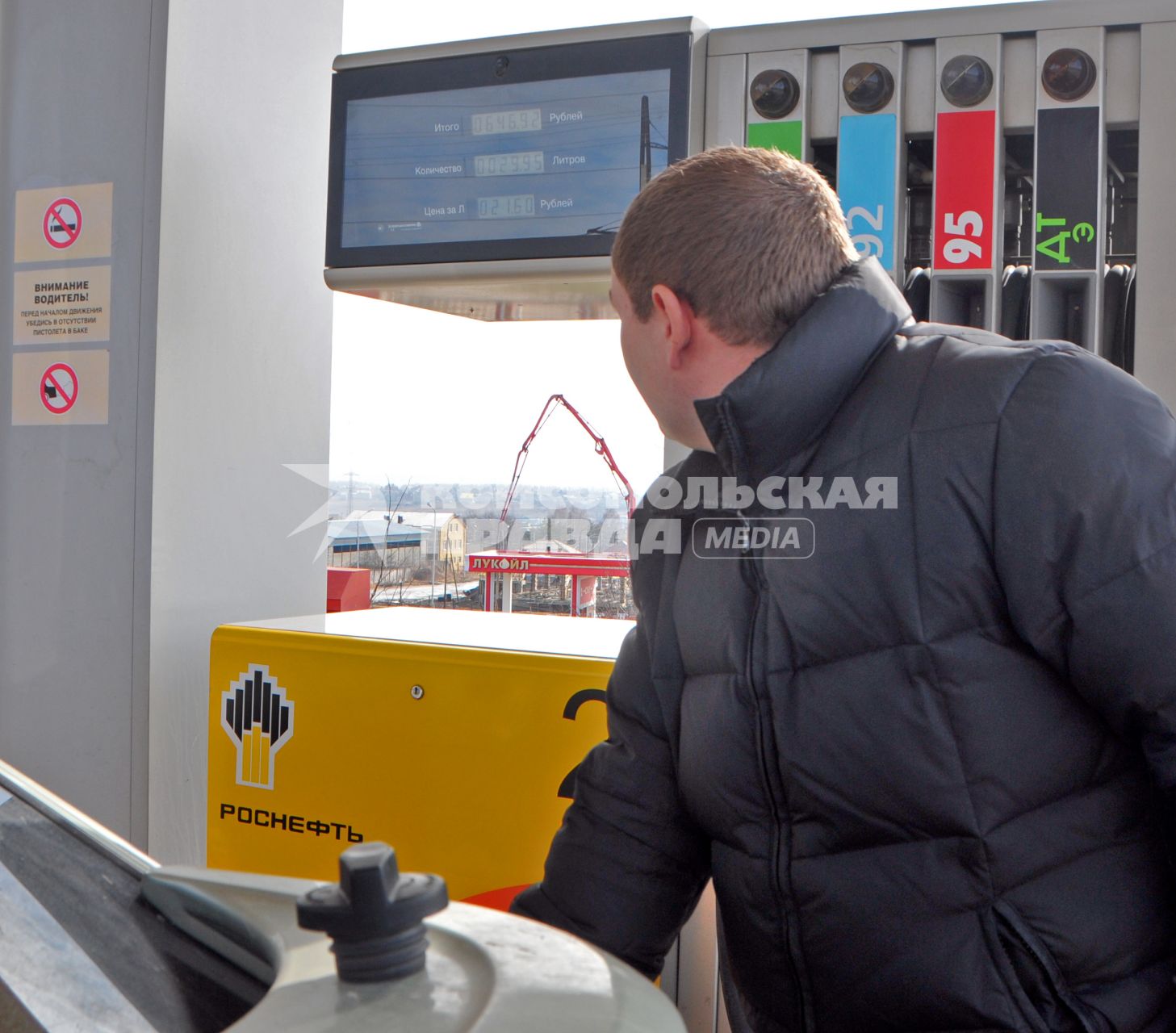 Мужчина заправляет автомобиль бензином, смотрит на табло колонки.