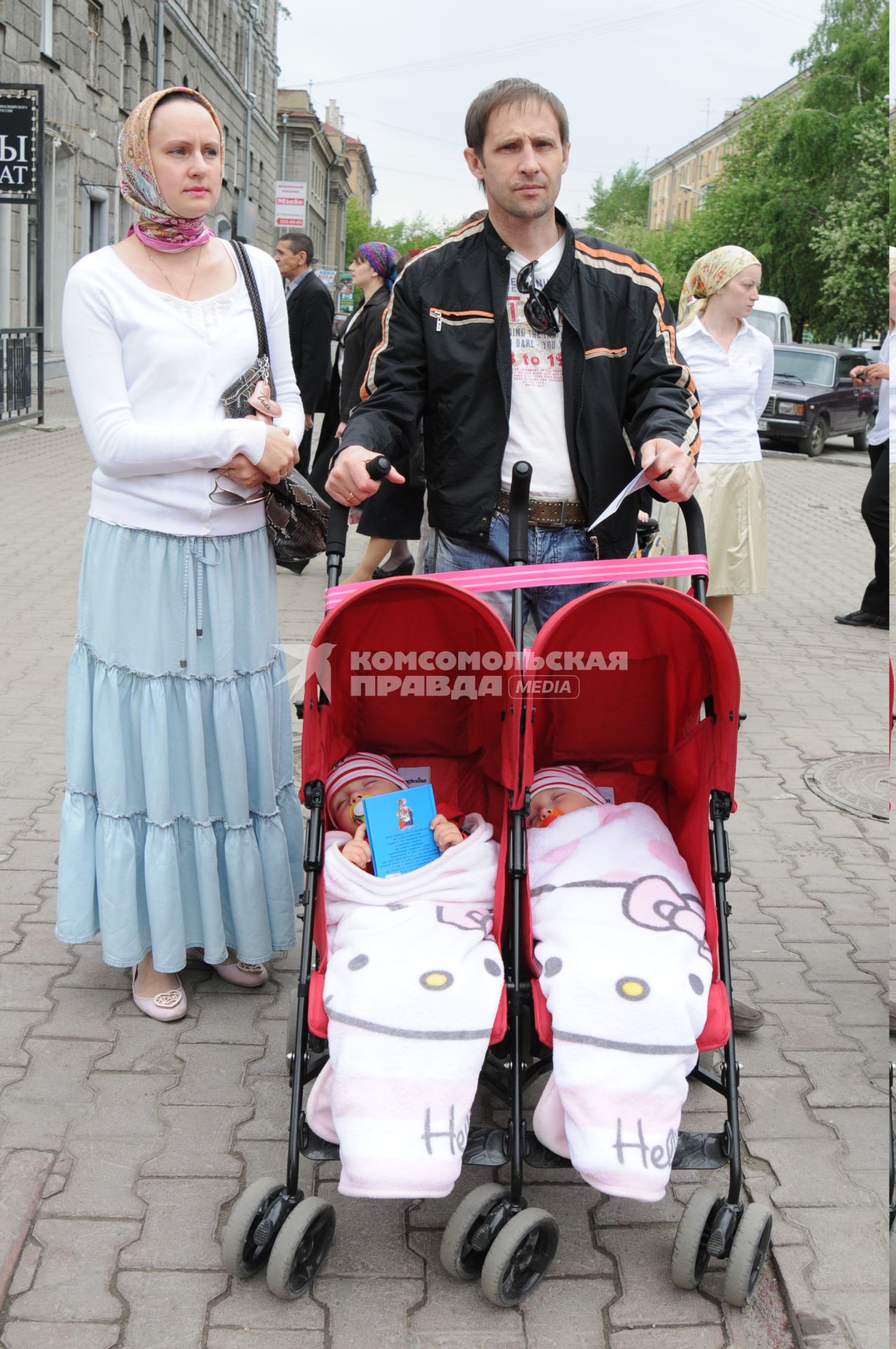 Мужчина с женщиной и двойняшками в детской коляске.