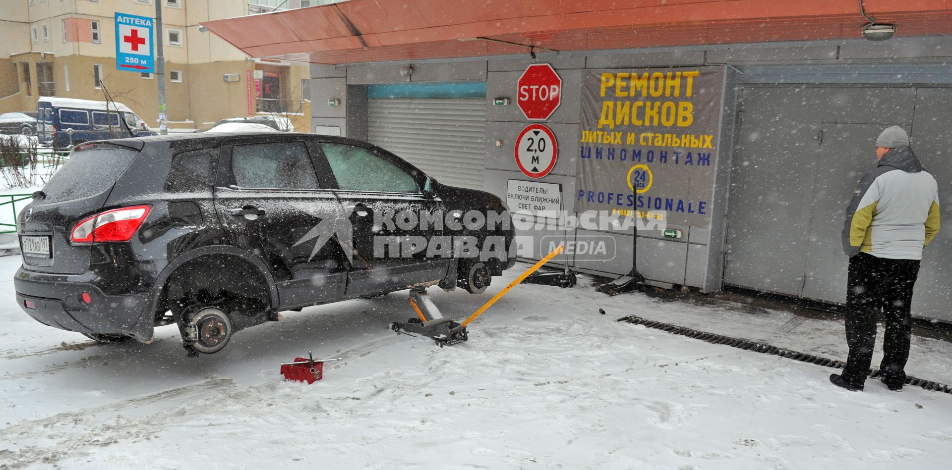 Мужчина около автосервиса переобувает свой автомобиль в зимнюю резину.