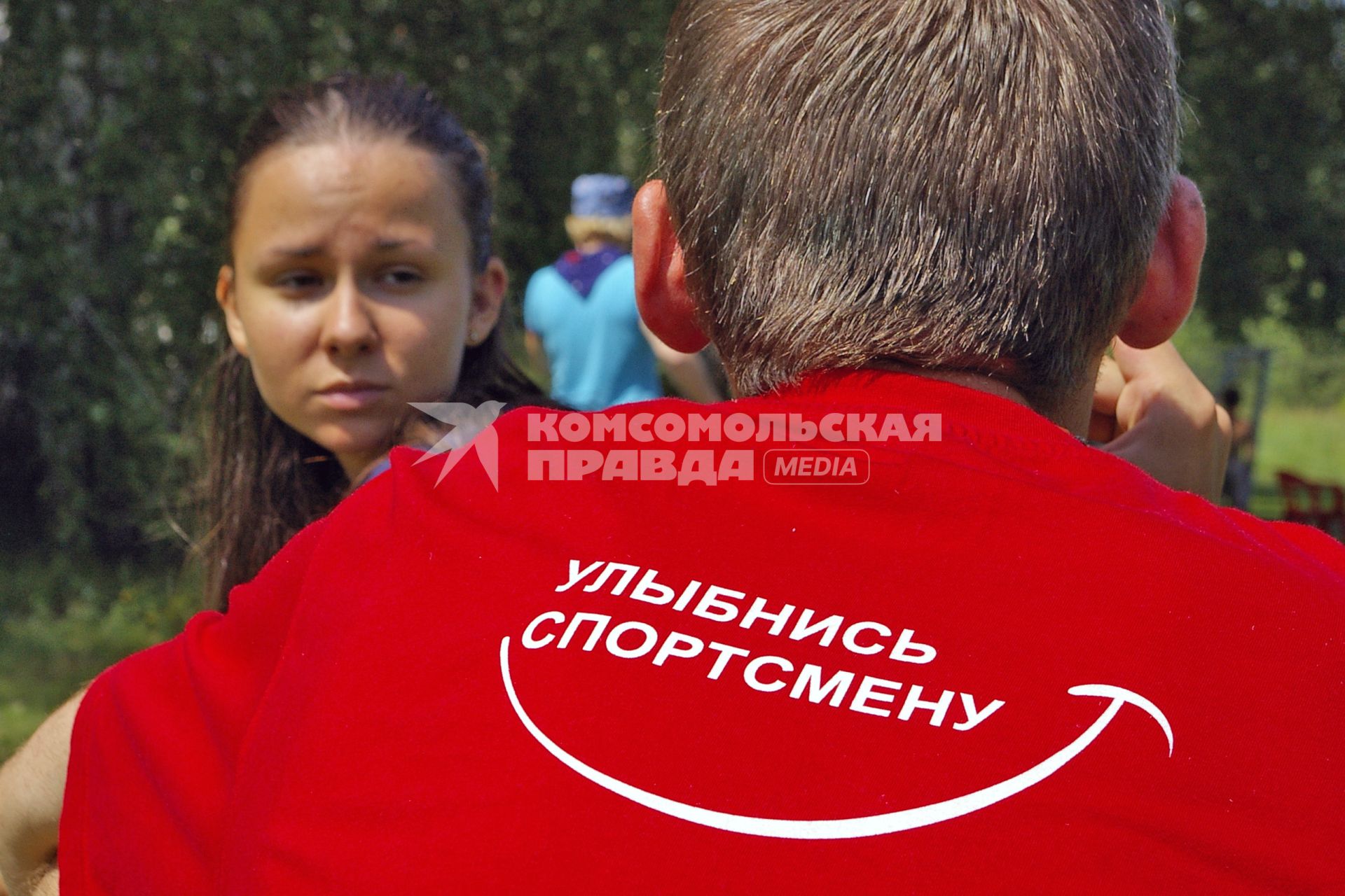 Девушка смотрит на юношу у которого на футболке надпись: `Улыбнись спортсмену`.