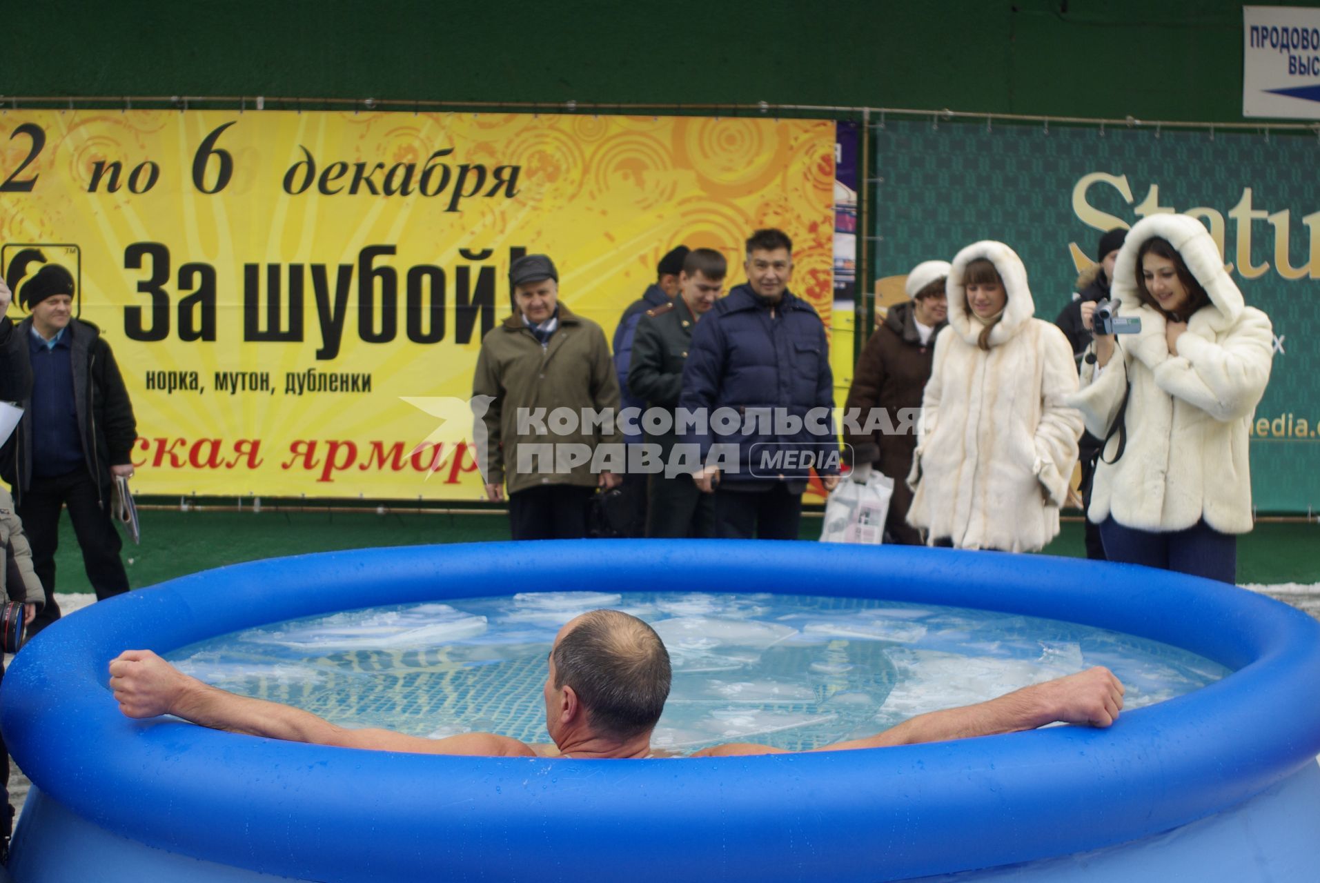 Мужчина в надувном бассейне плавает, рядом стоят тепло одетые люди.