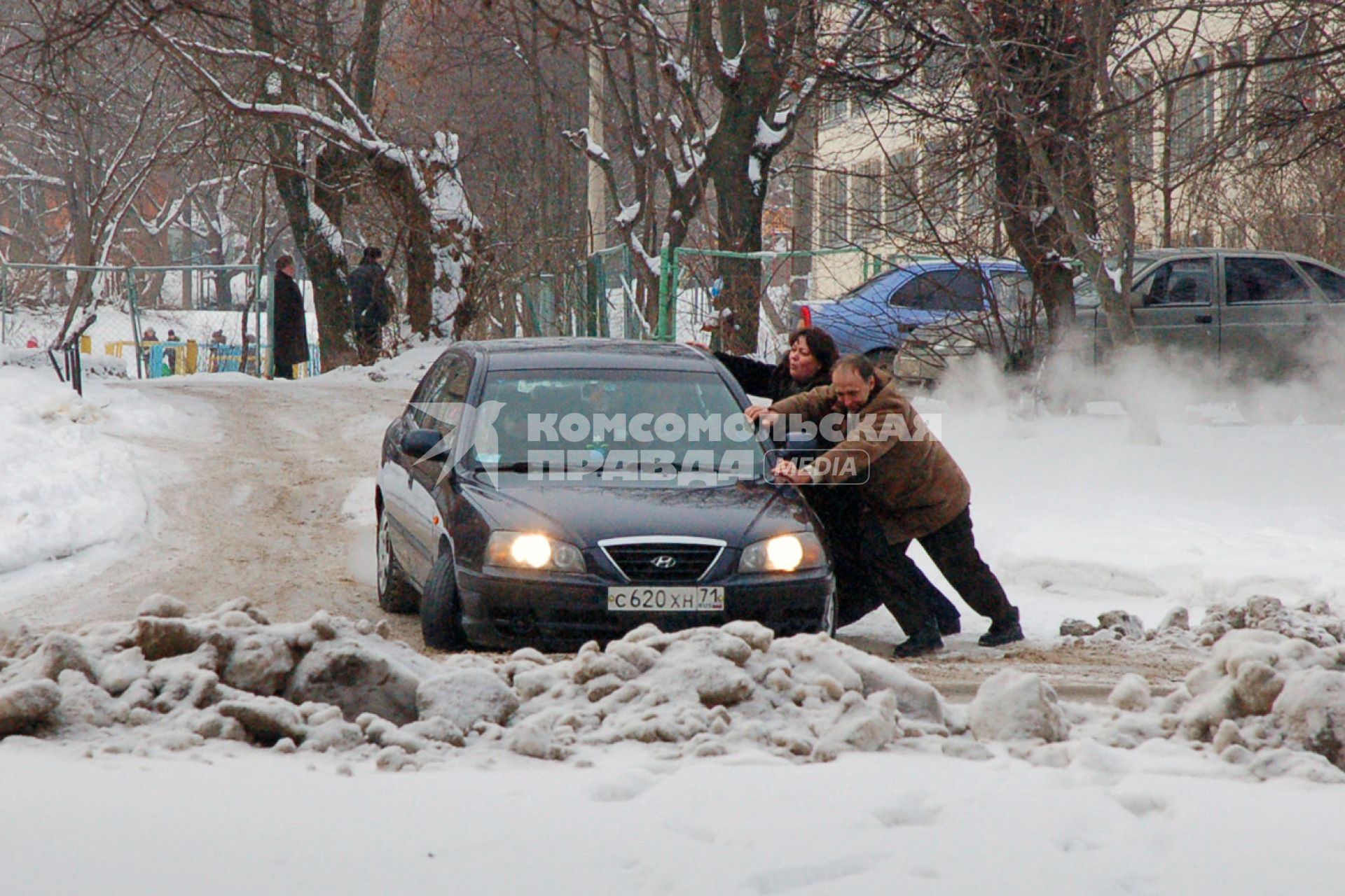 Мужчина и женщина выталкивают легковой автомобиль из сугроба.