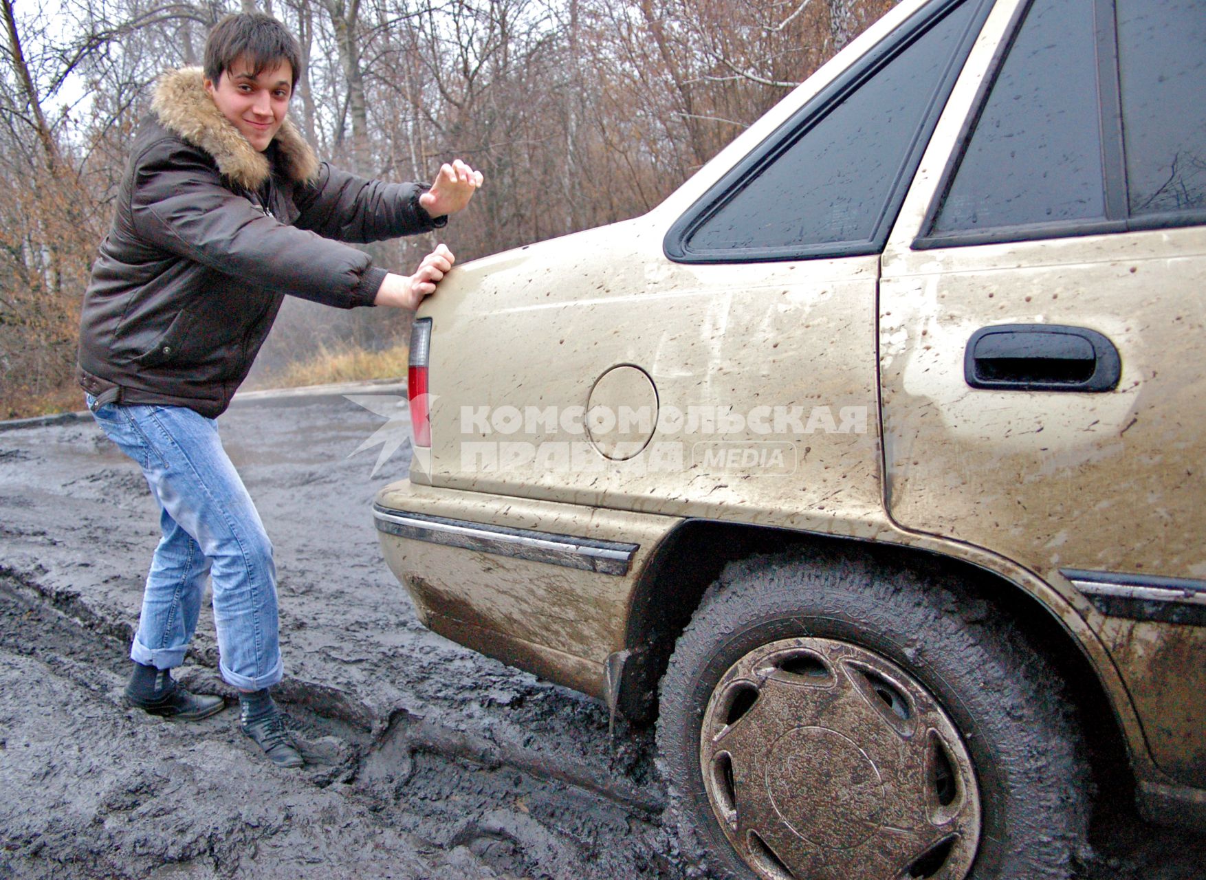 Парень толкает машину, застрявшую в грязи.