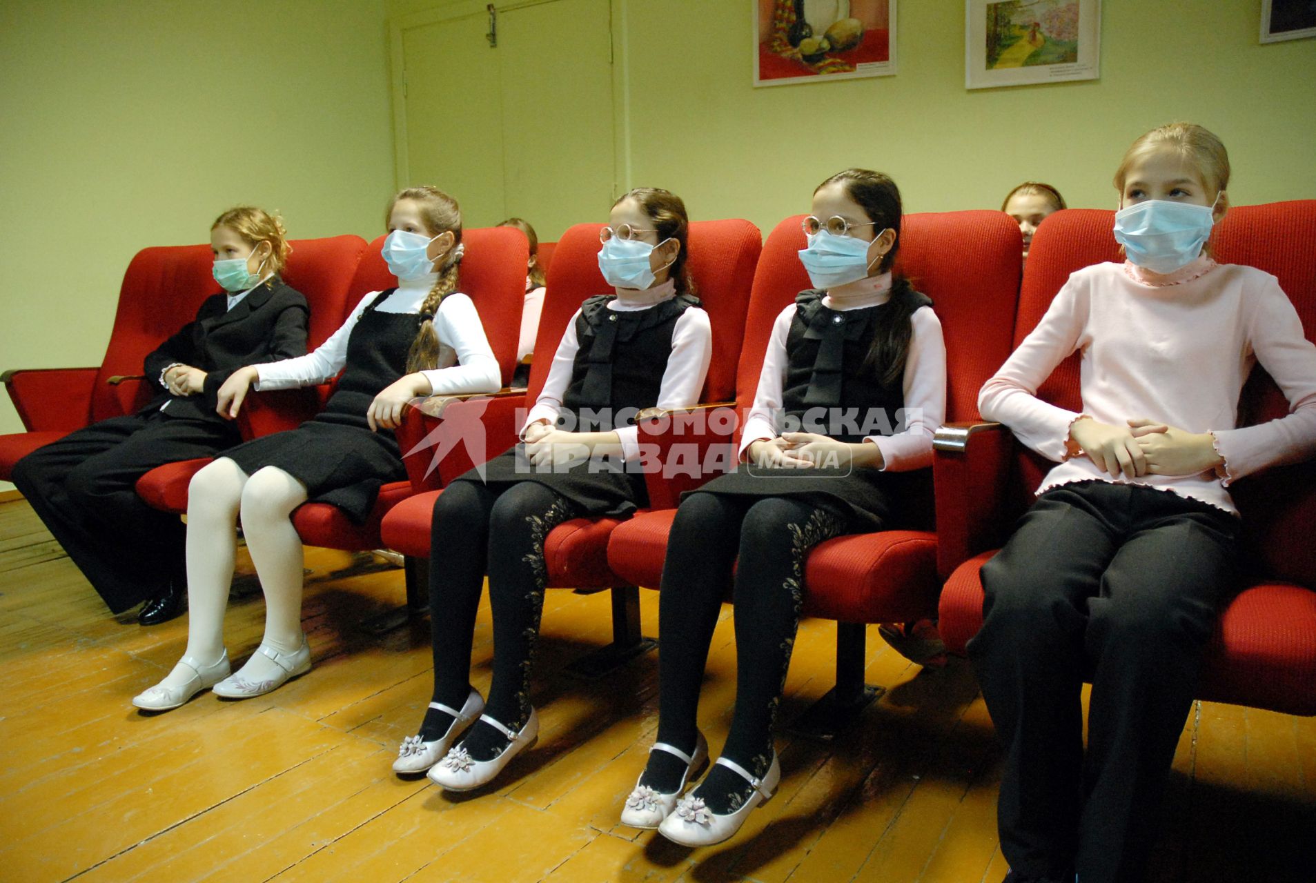 Школьники в медицинских повязках сидят в креслах в кабинете просмотра учебных фильмов.