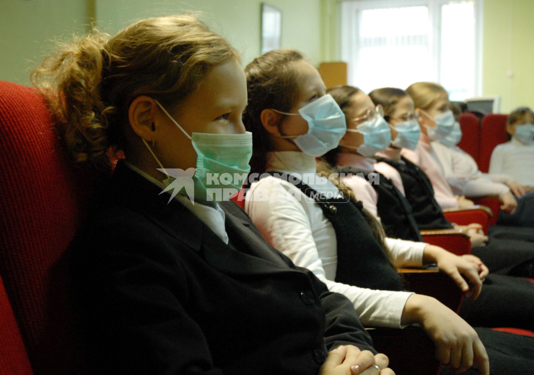 Школьники в медицинских повязках сидят в креслах в кабинете просмотра учебных фильмов.