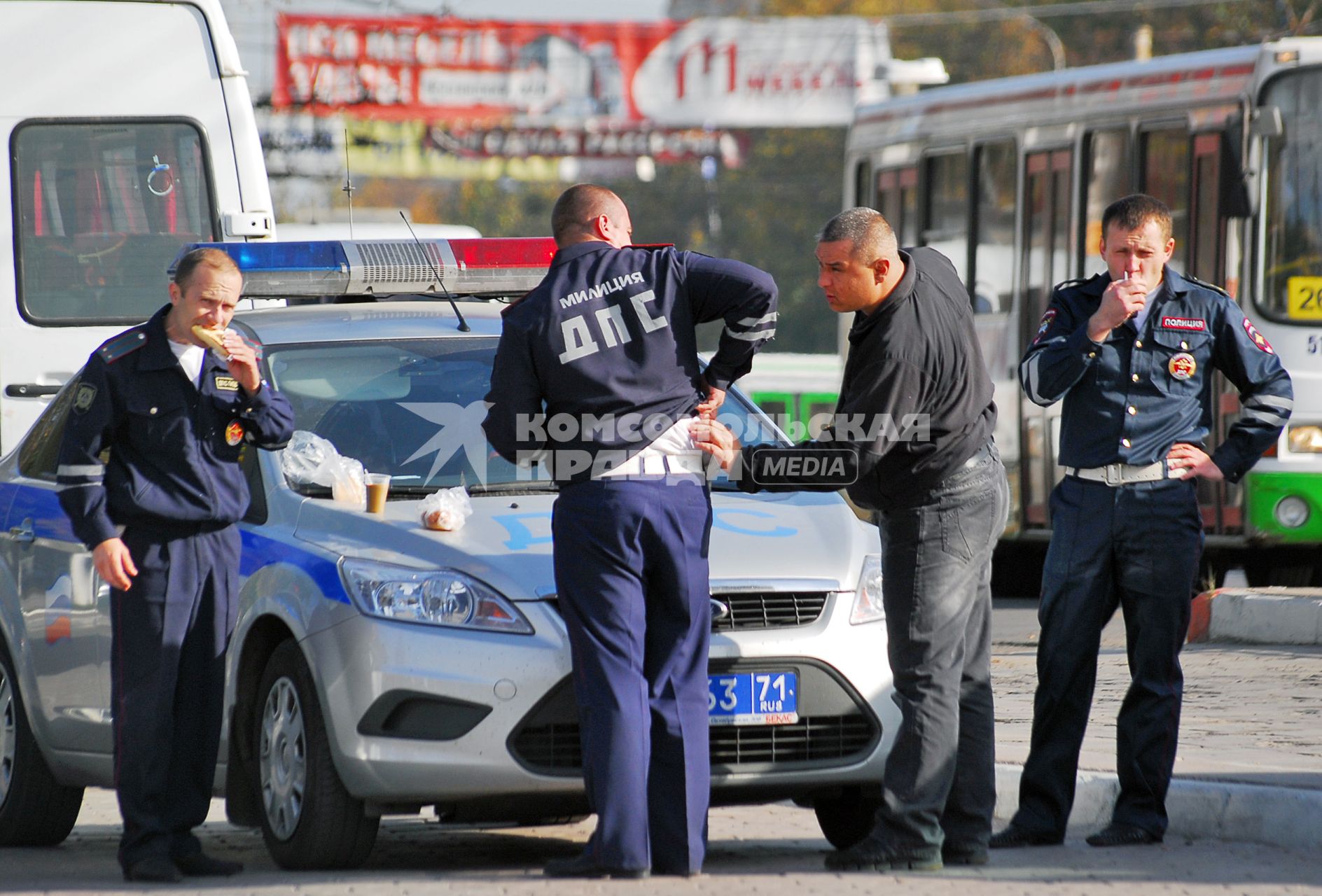Сотрудники ДПС ГИБДД едят на улице, фастфуд разложен на капоте патрульной машины.