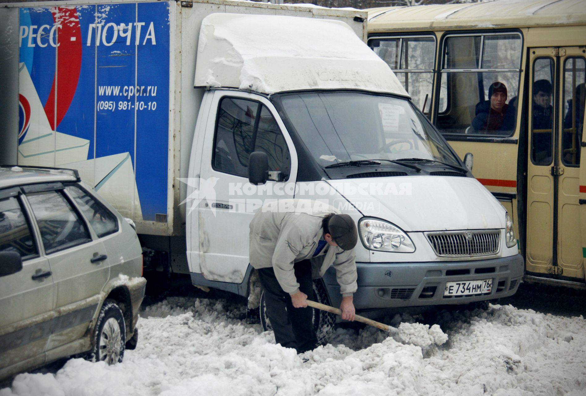 Мужчина отчищает автомобиль от снега с помощью деревянной лопаты.