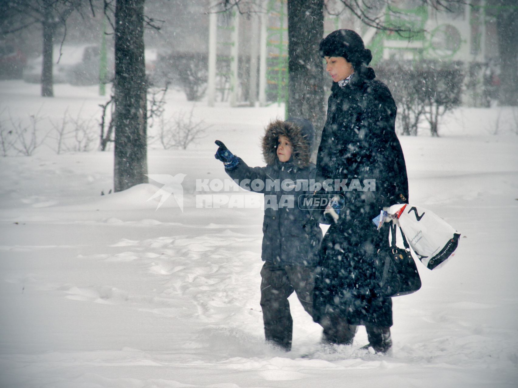 Во время снегопада женщина с ребенком идут по улице.