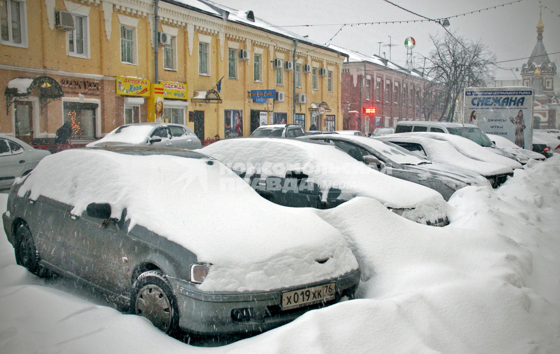 Автомобили засыпанные снегом стоят на улице города.